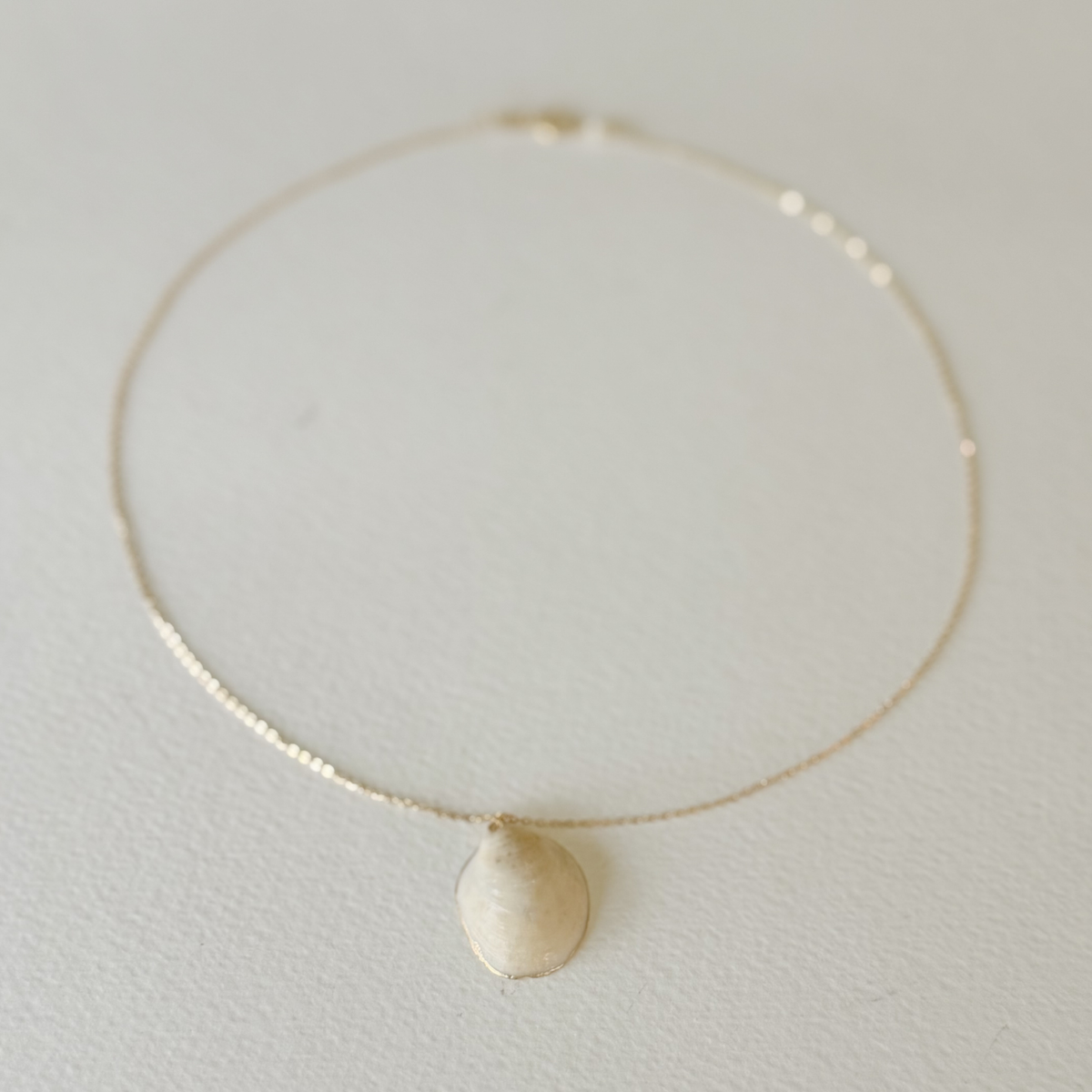 Gold necklace with a round pendant on a light gray background