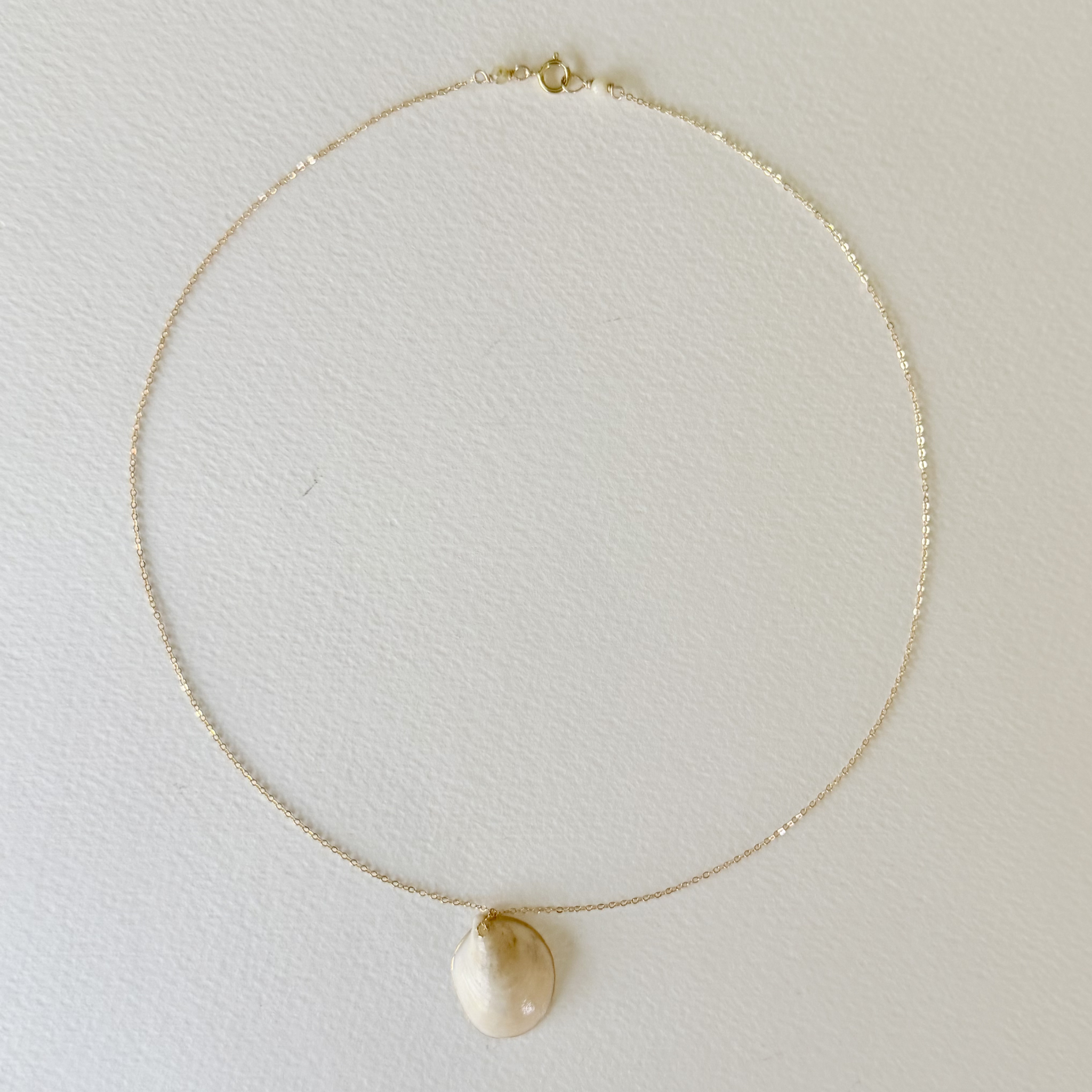 Gold necklace with a teardrop-shaped pendant on a light gray background