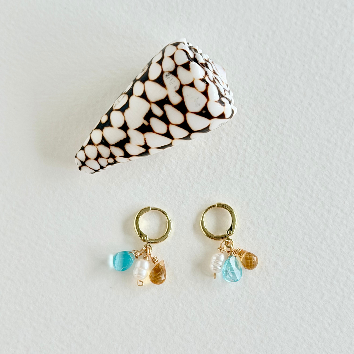 Pair of gold earrings with blue and pearl drops on a light gray background