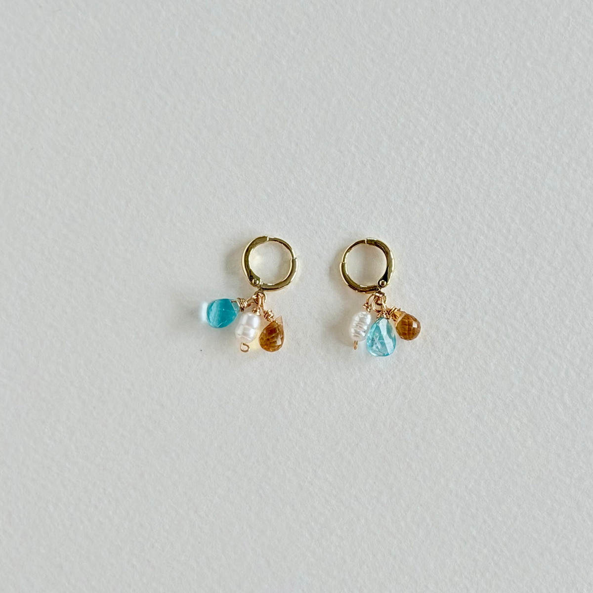 Pair of gold earrings with colorful beads on a light gray background