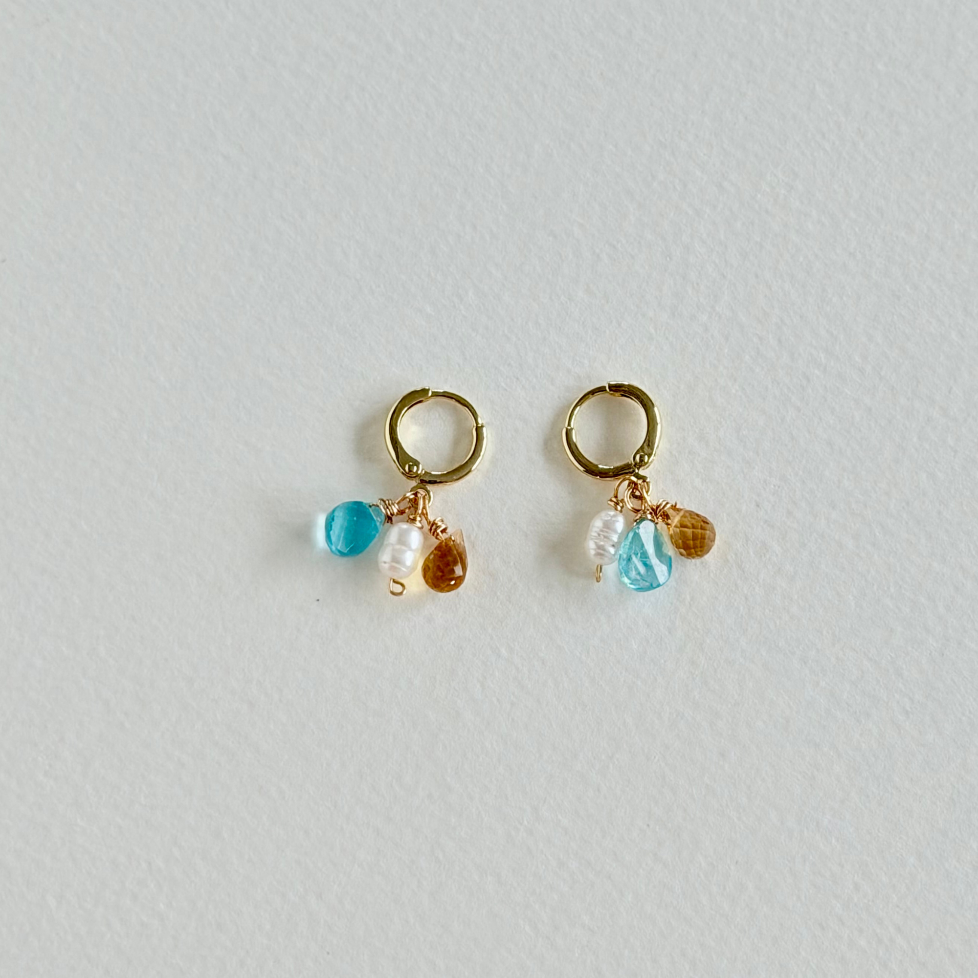 Pair of gold earrings with blue and brown beads on a light gray background