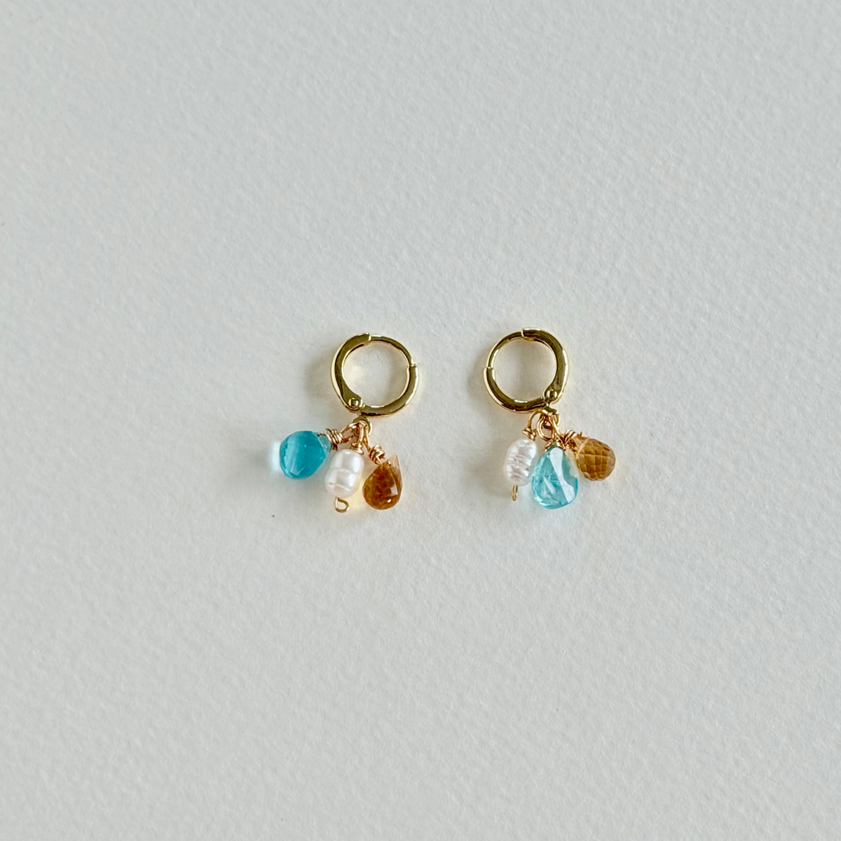 Pair of gold earrings with blue and brown beads on a light gray background