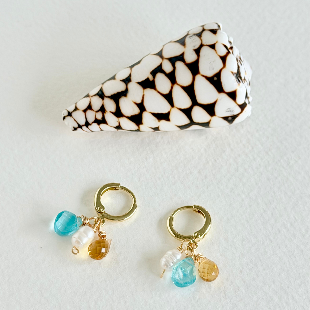 Pair of gold hoop earrings with blue and gold charms on a white background
