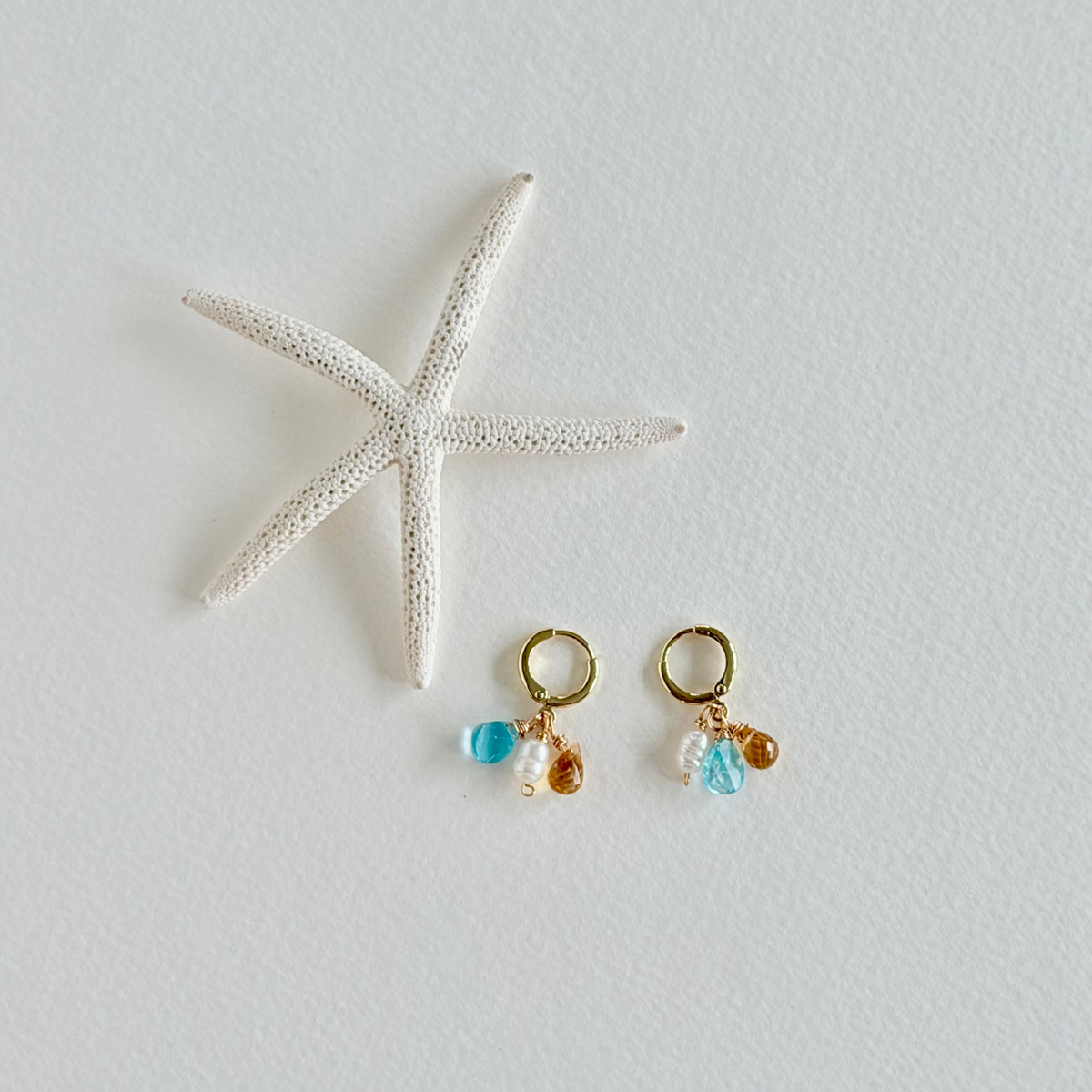 Pair of gold earrings with blue and clear beads on a light gray background with a starfish.