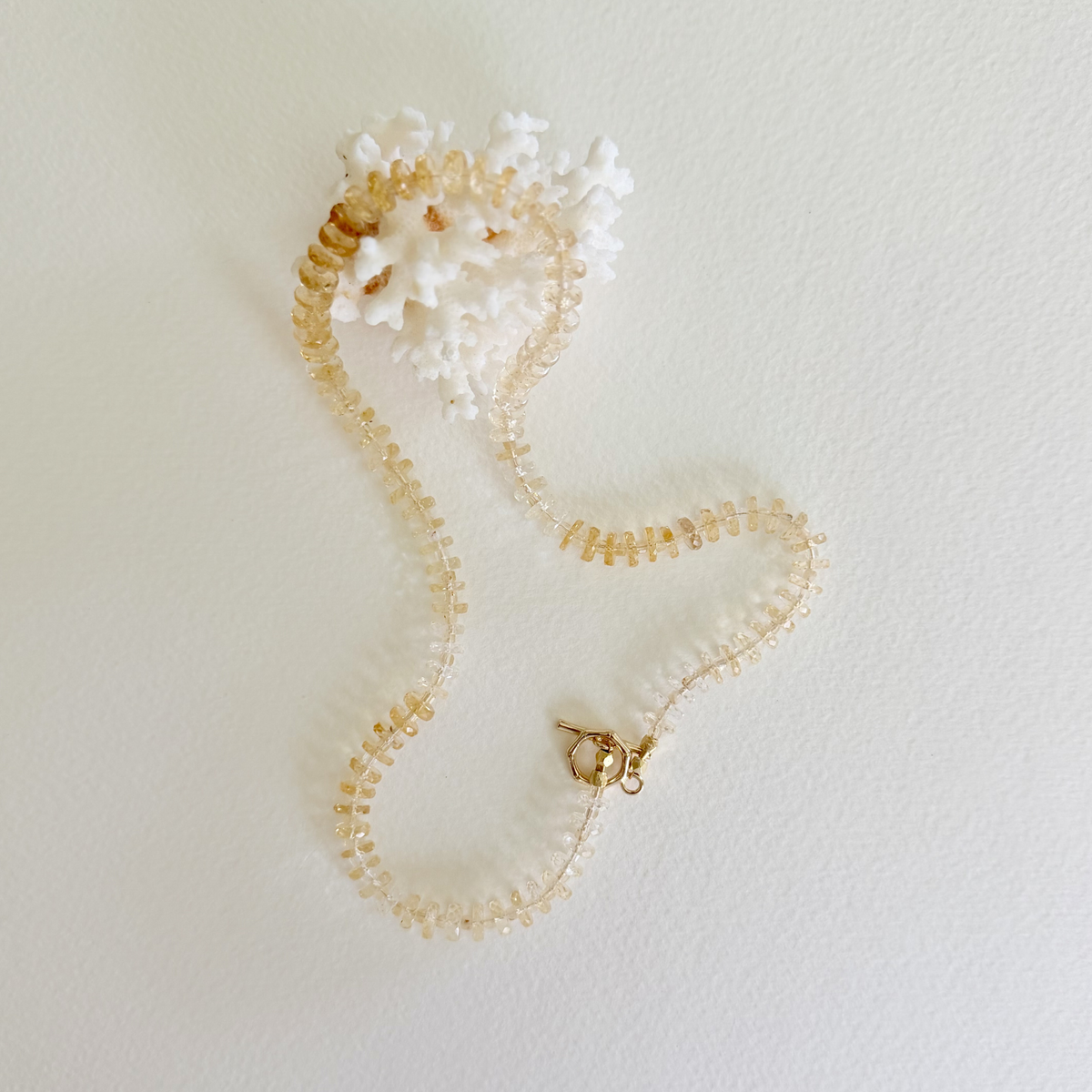 Handmade coastal-inspired jewelry featuring turquoise, freshwater pearls, and 14k gold-filled details in golden hour sunlight. Styled on a piece of coral