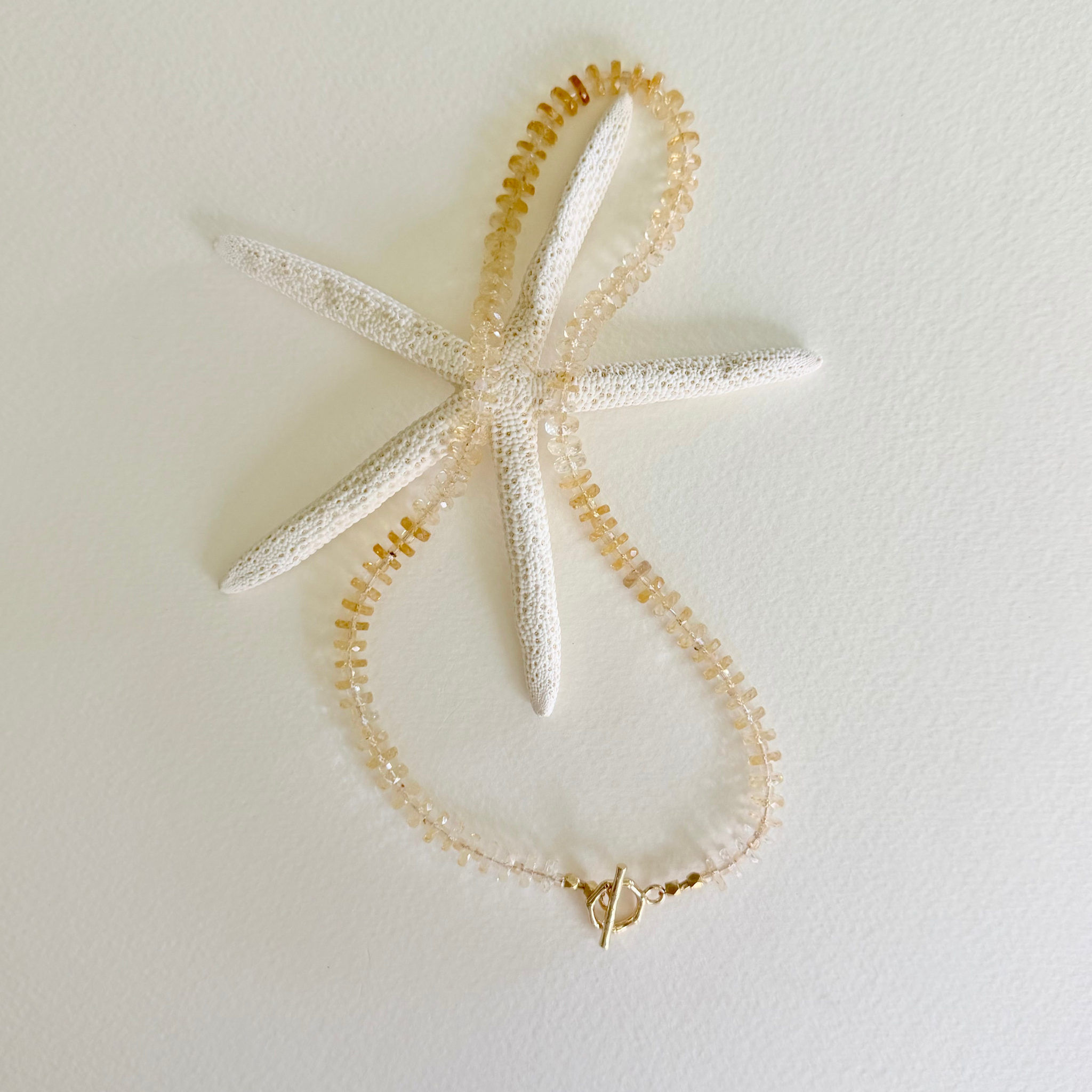 Golden Hour Citrine Necklace handcrafted with natural faceted citrine gemstones in a champagne-to-honey ombré and finished with a 14k gold-filled toggle clasp styled on a white background with a starfish.