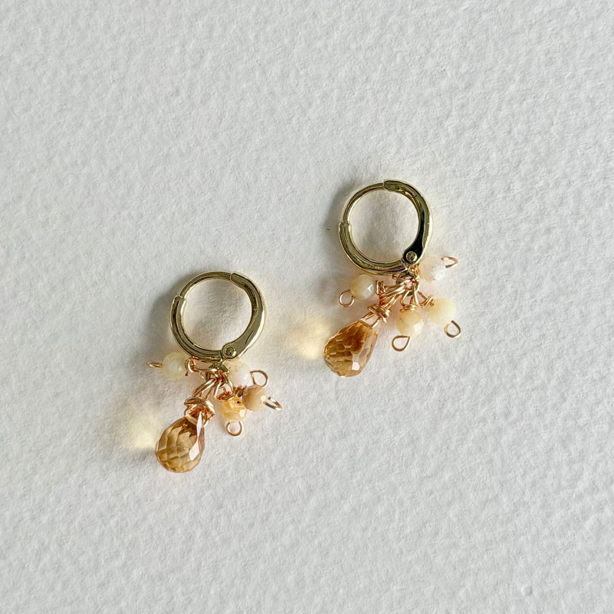 Gold hoop earrings with small gemstones on a light gray background