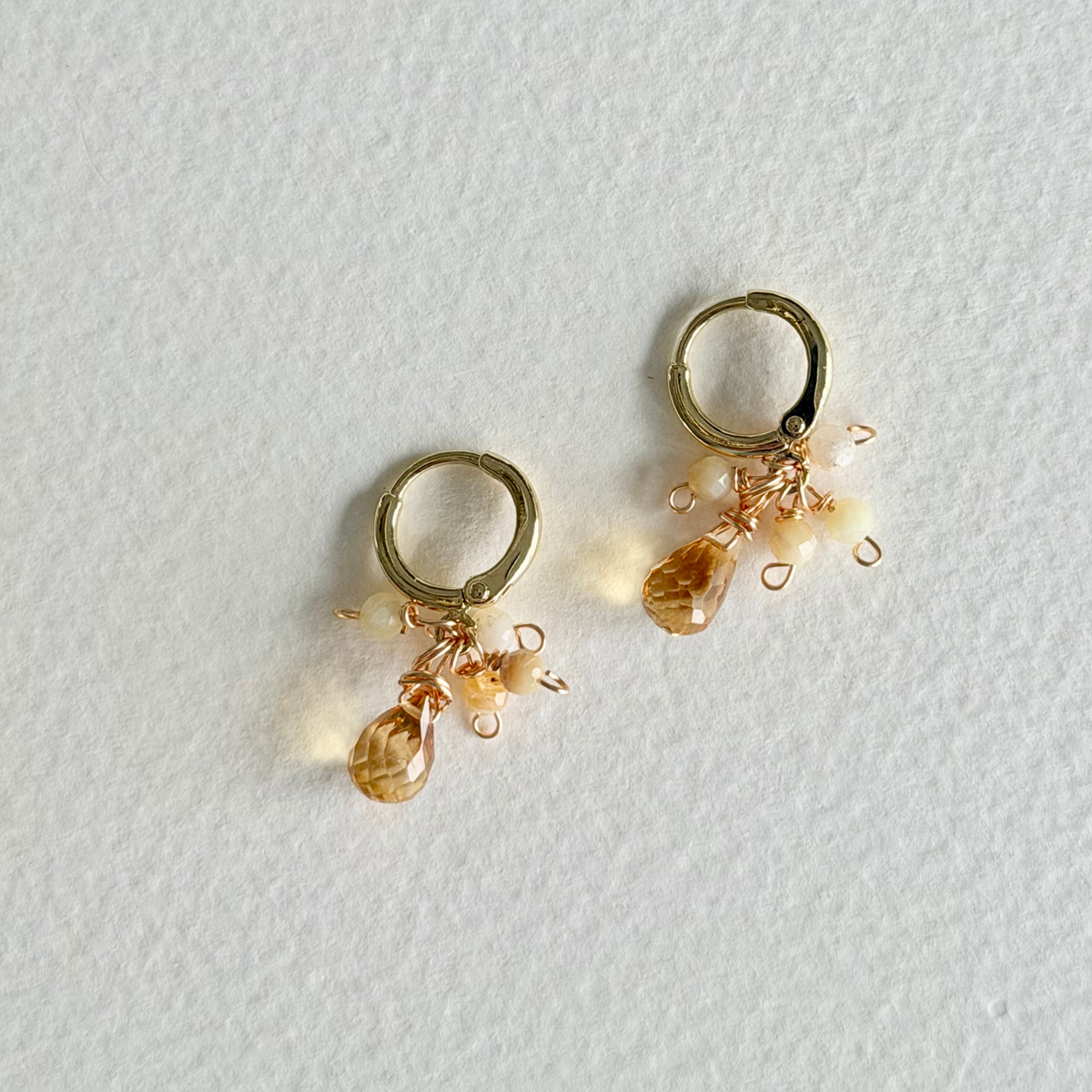 Gold hoop earrings with bead drops on a light gray background