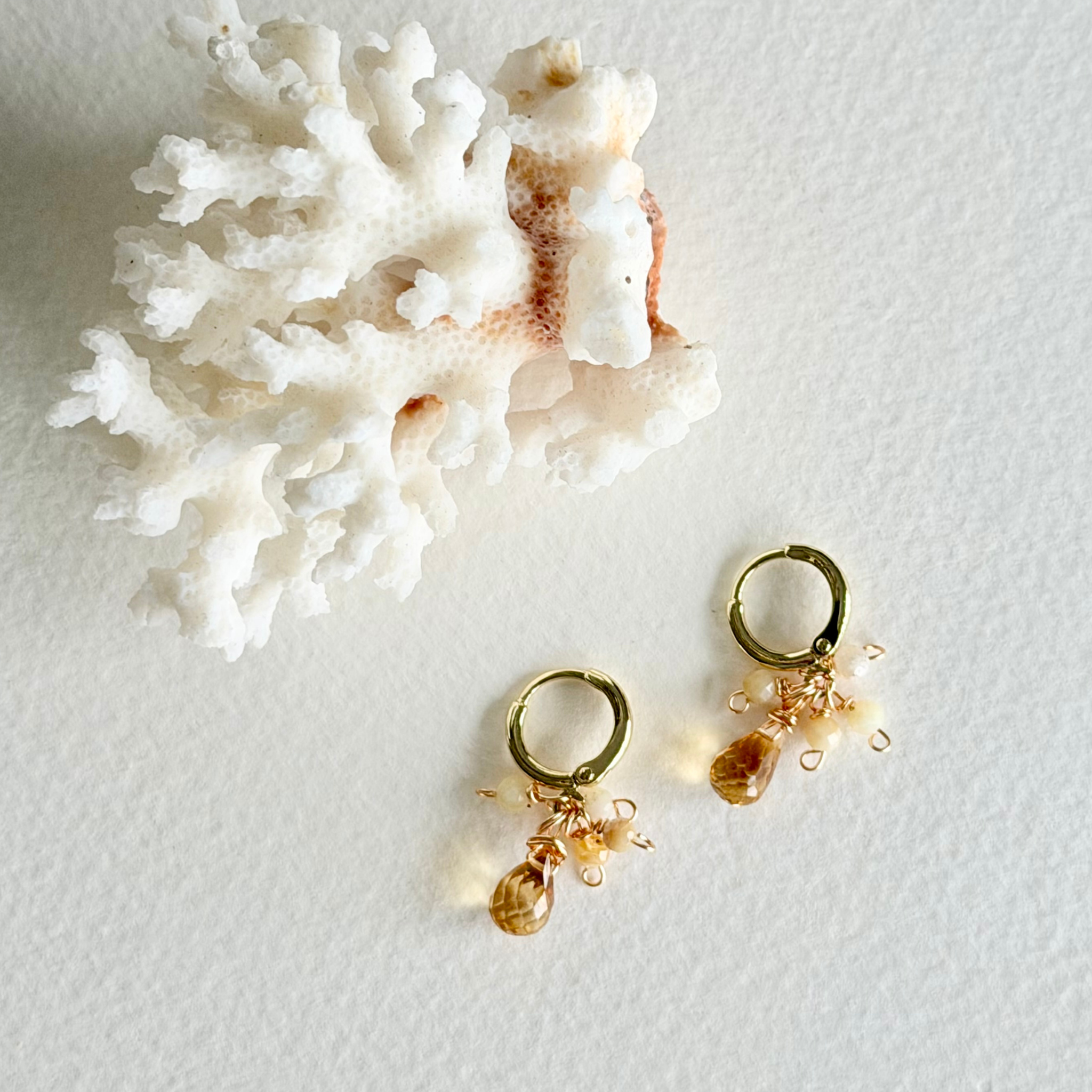 Gold earrings with small stones on a white surface with coral