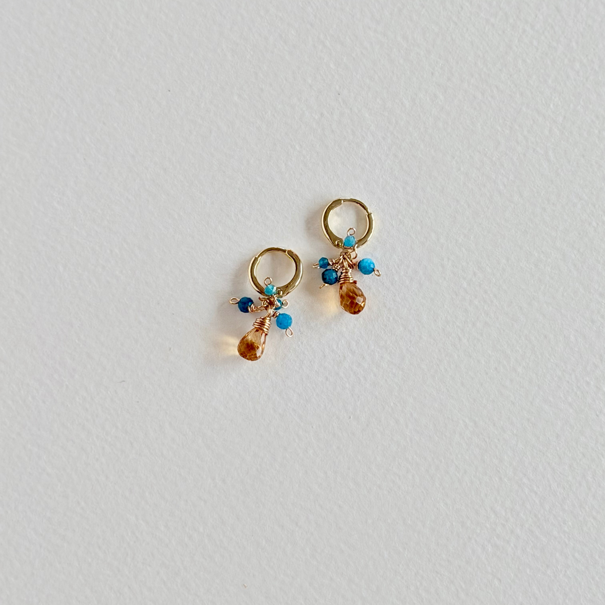 Pair of gold earrings with gemstones on a light gray background