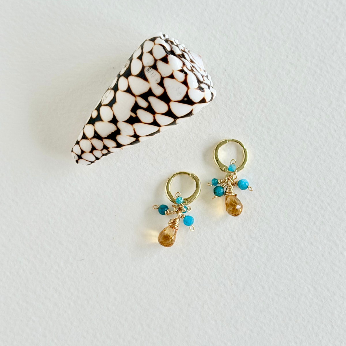 citrine and turquoise huggie hoop earrings on light background styled with a shell