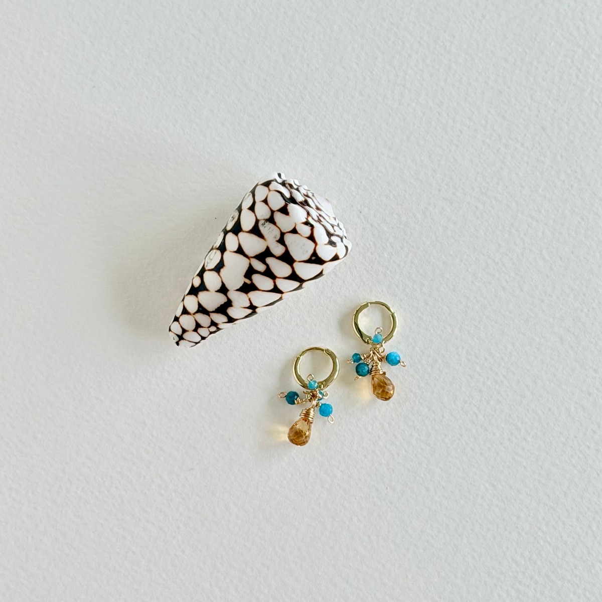 Pair of gold and turquoise earrings on a light gray background with a decorative shell.