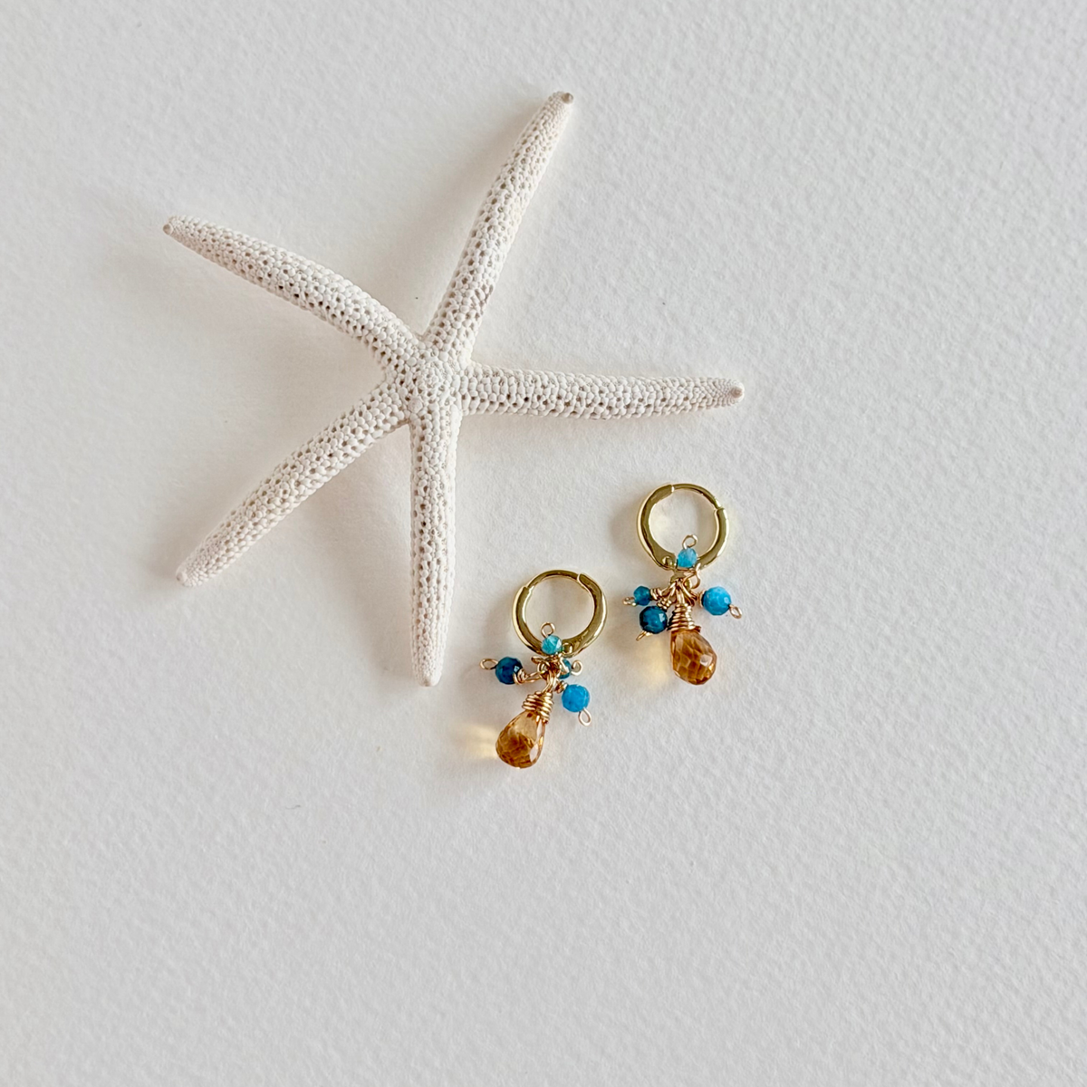 Pair of earrings with gemstones on a white surface with a starfish.