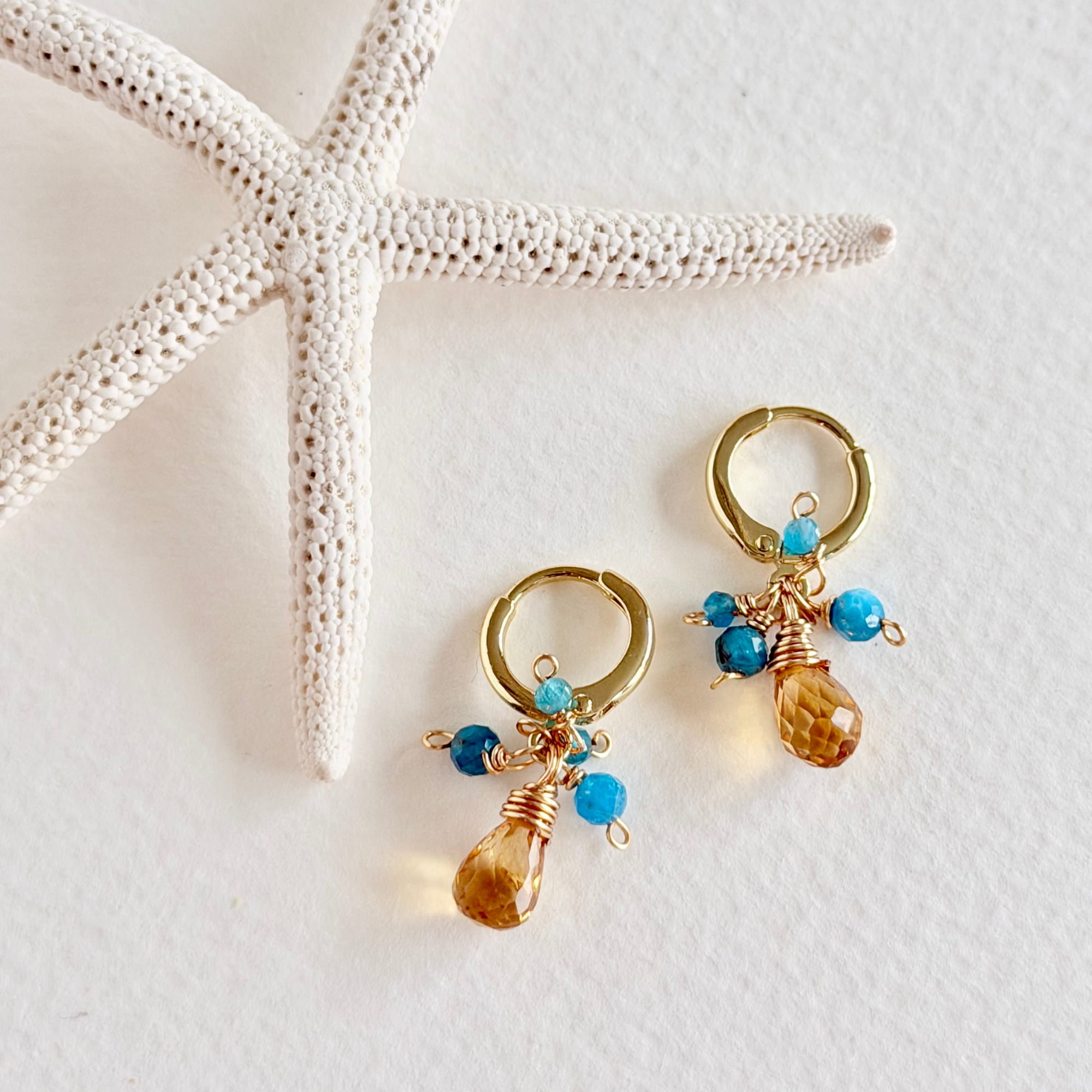Gold hoop earrings with blue and brown beads on a white surface with starfish