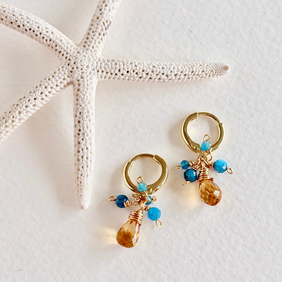 Gold hoop earrings with blue beads on a white surface with starfish