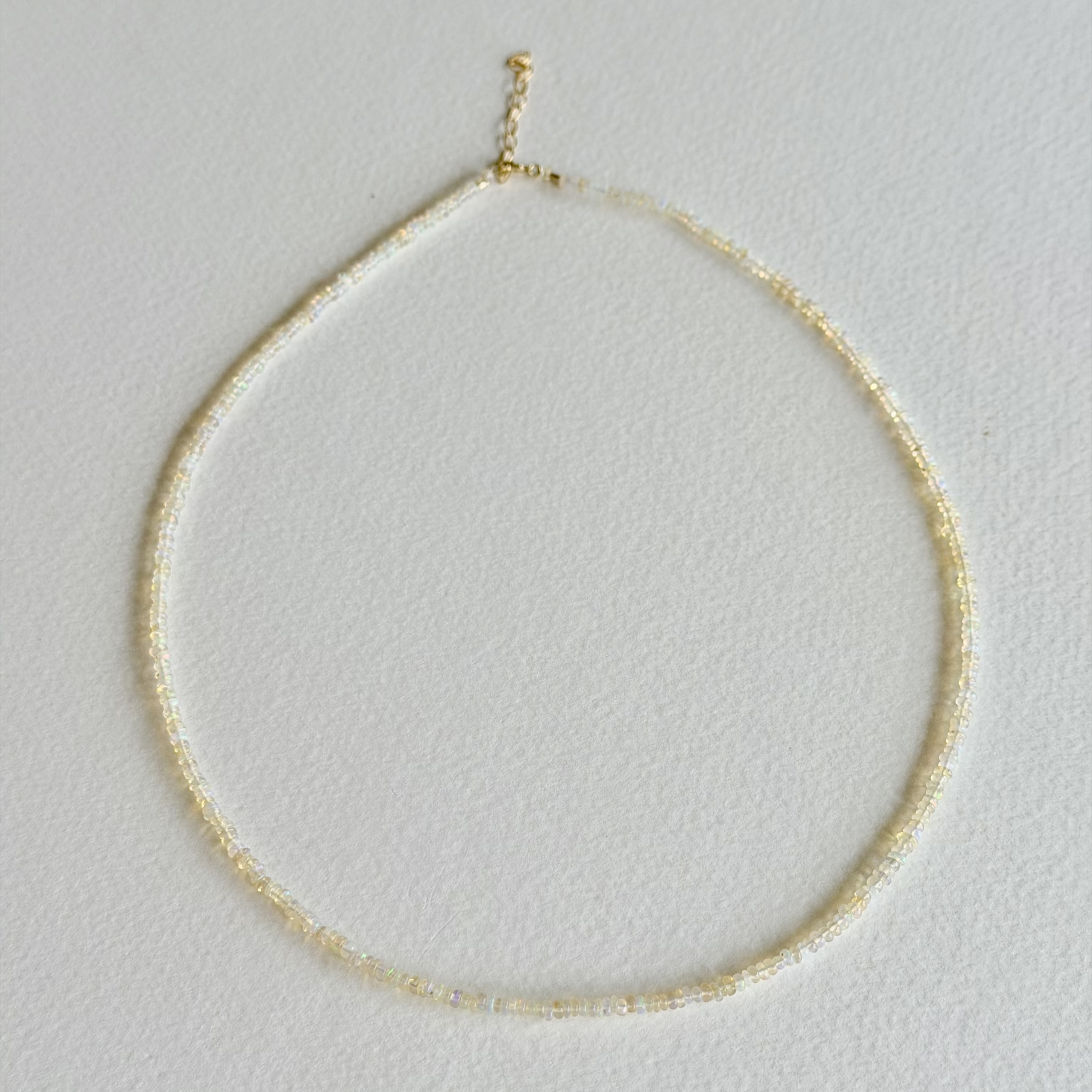 A delicate gold beaded necklace arranged in a circle on a textured white background.