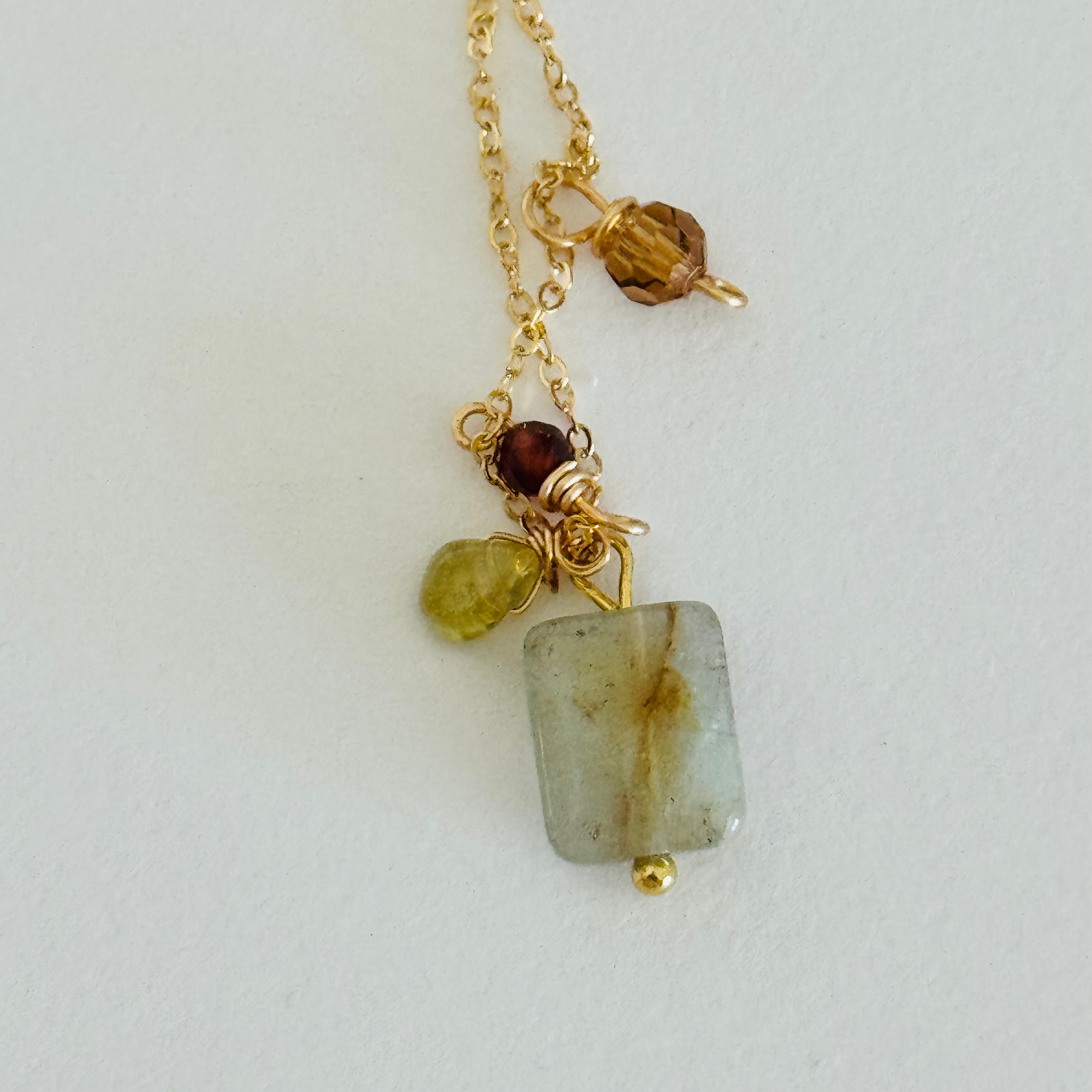 Close up of aventurine, peridot, and garnet hessonite beads on gold chain necklace on white surface.