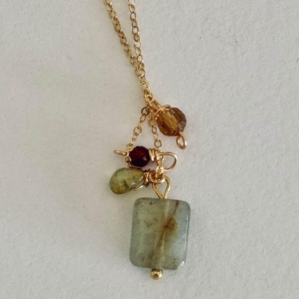 Simple chain necklace with one each of aventurine, peridot, and garnet hessonite beads in warm fall coastal colors. Close up view on white surface.