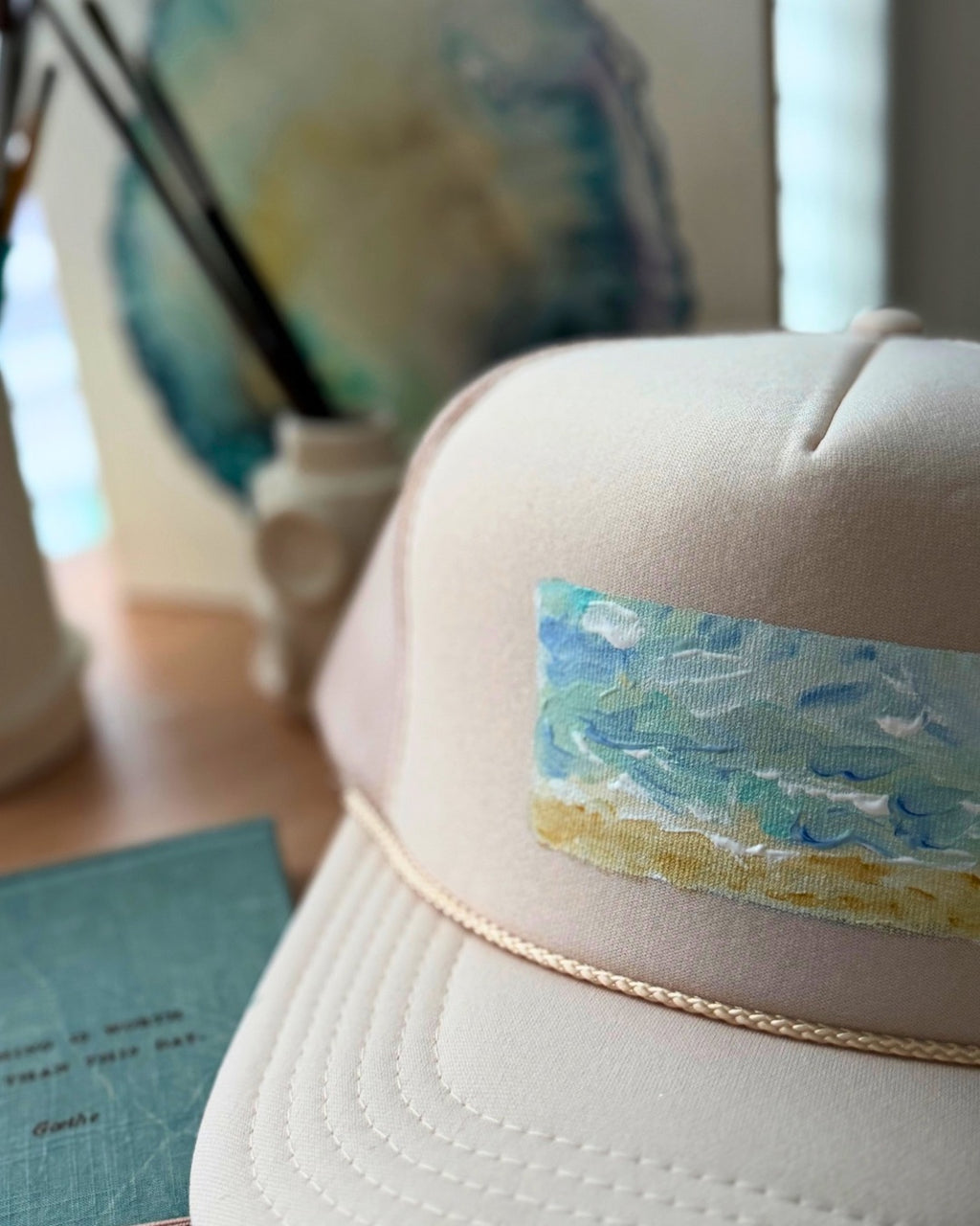 Close up of Cream hand-painted trucker hat featuring original textured ocean artwork in turquoise, blue and sandy gold by Marie & Oakley.