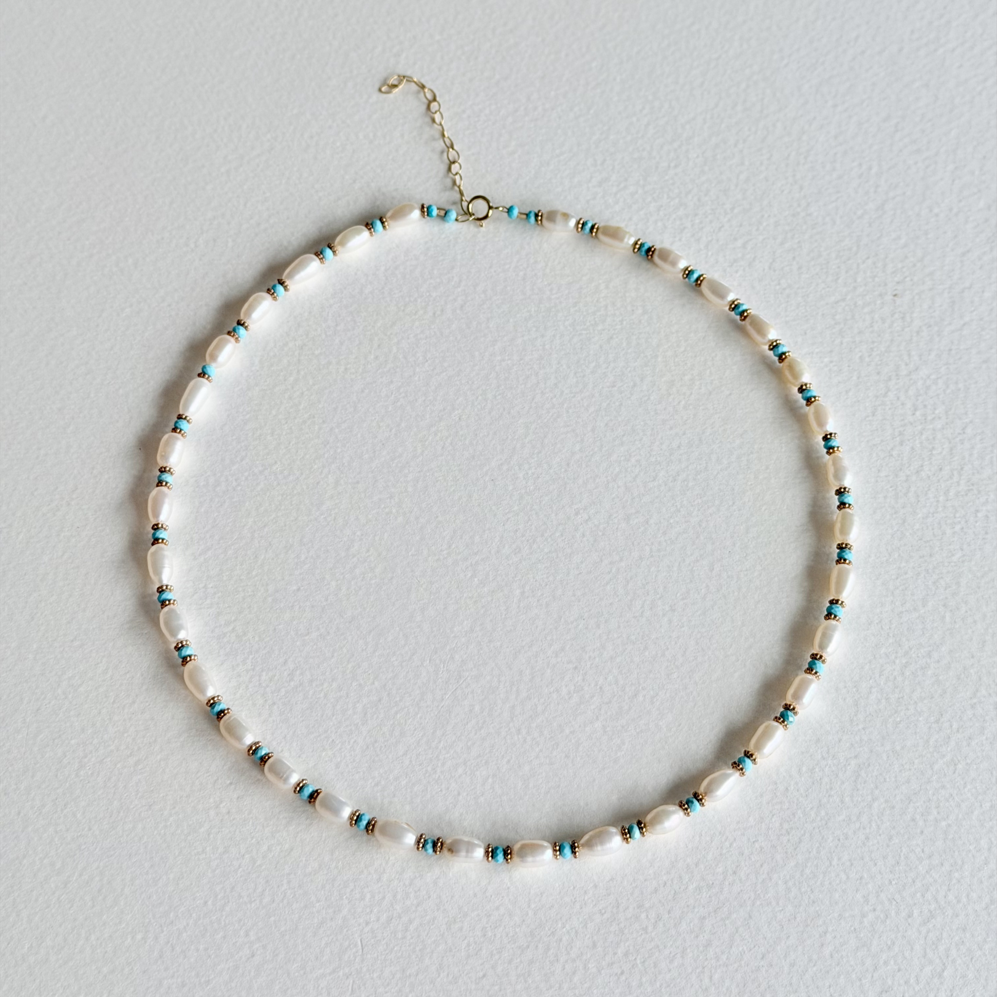 A beaded necklace with irregular white shell-like beads and small turquoise-blue spacer beads, arranged in a circle on a light gray background.