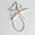 A beaded necklace with white shell-like beads and small turquoise and dark blue spacer beads, displayed on a white starfish prop against a white background.