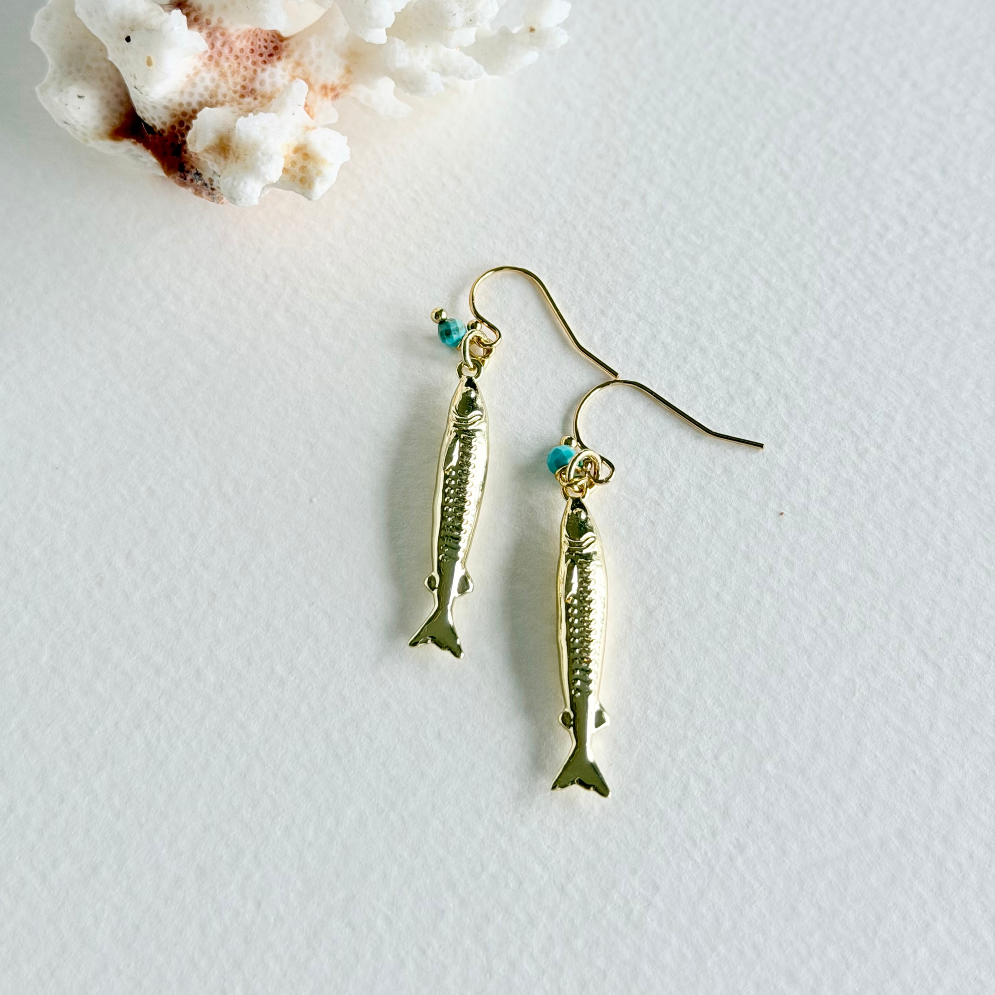 Gold fish-shaped earrings on a light background with coral.