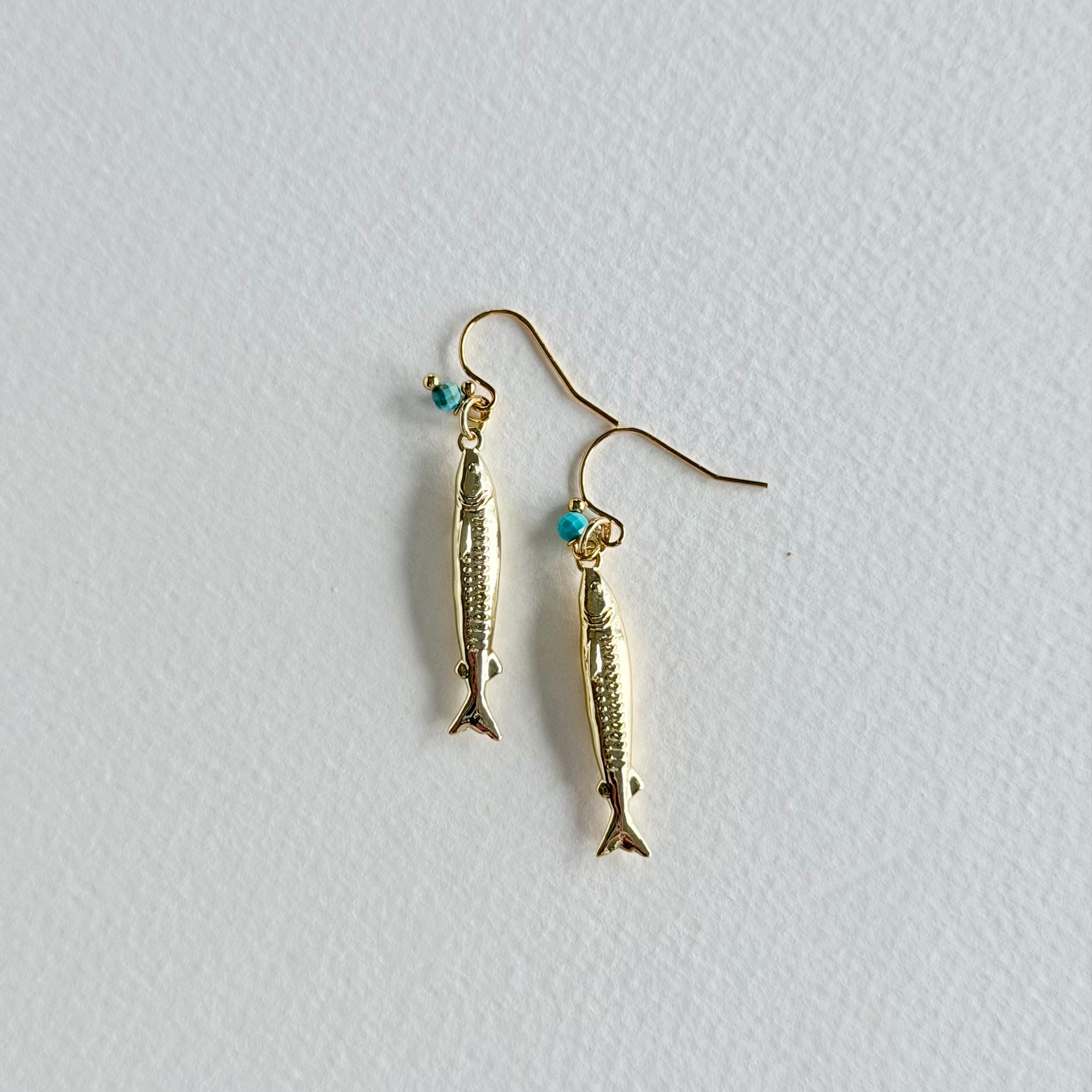 Gold fish-shaped earrings on a light gray background