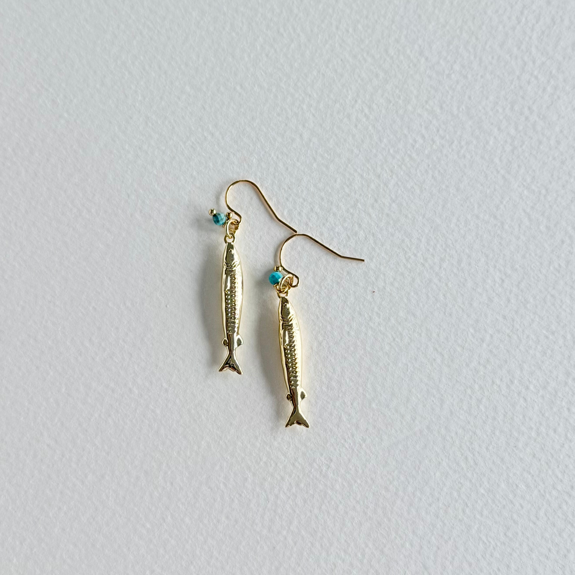 Gold fish-shaped earrings on a light gray background