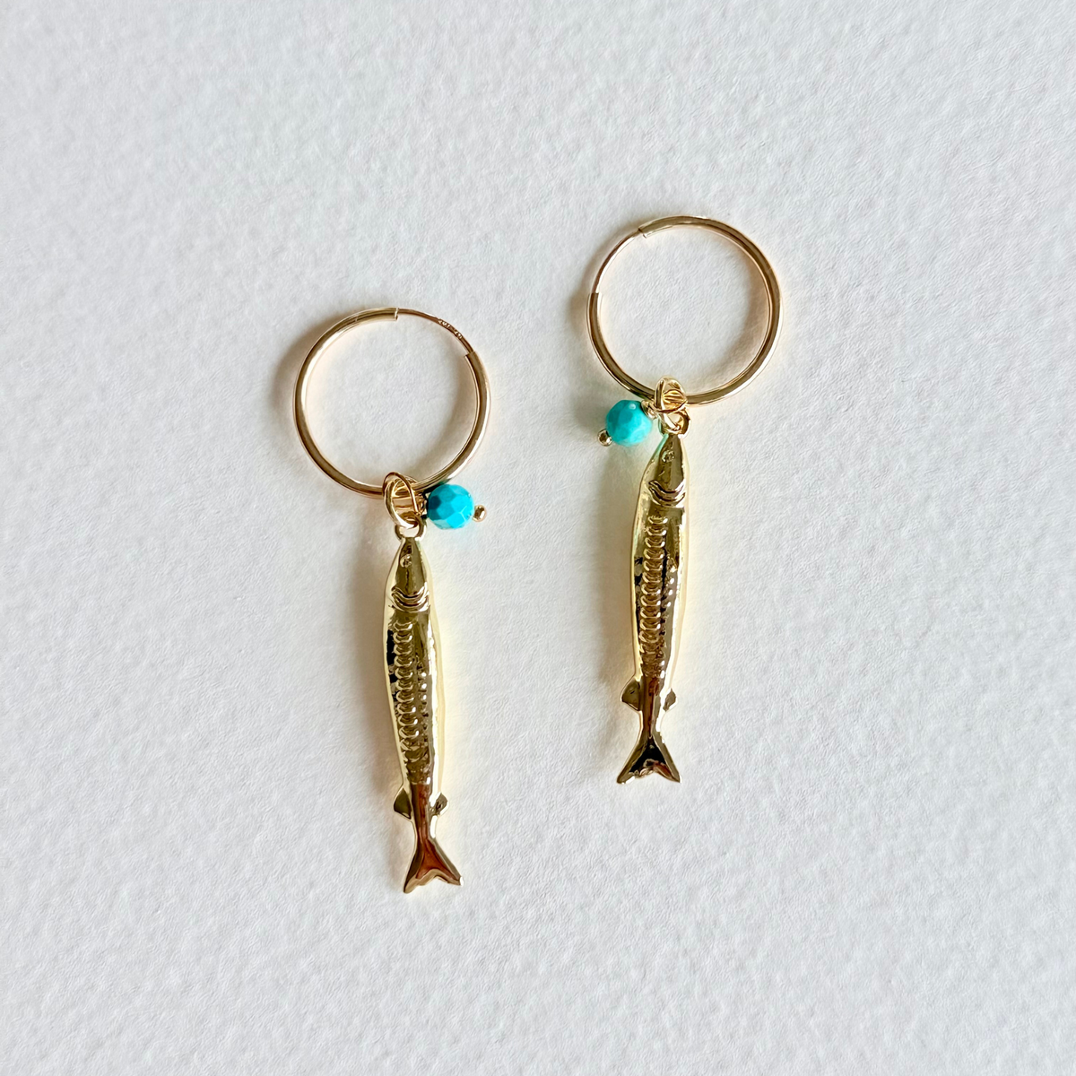 Gold fish-shaped earrings with turquoise beads on a white background