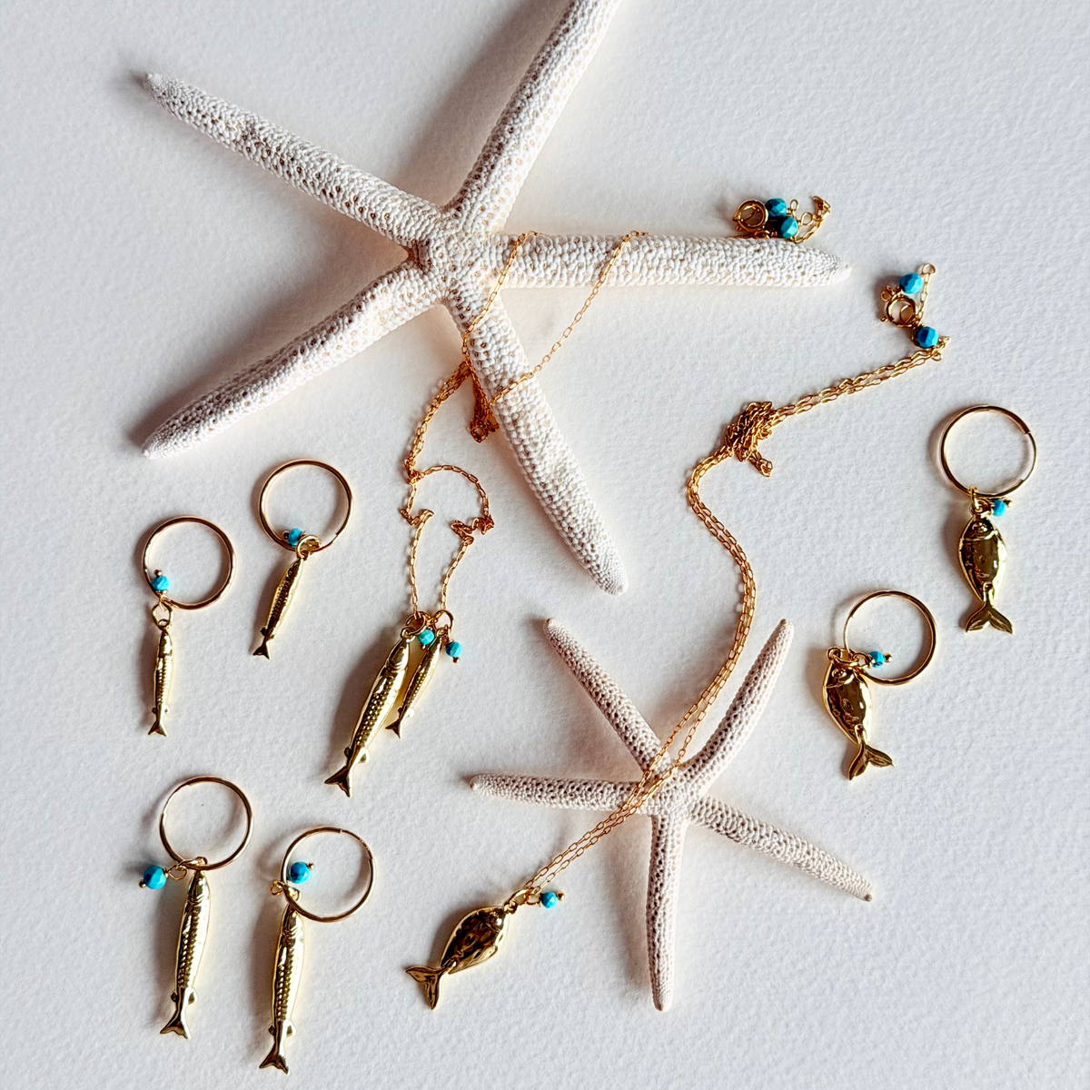 Gold fish-shaped keychains with turquoise beads on a white surface with starfish.