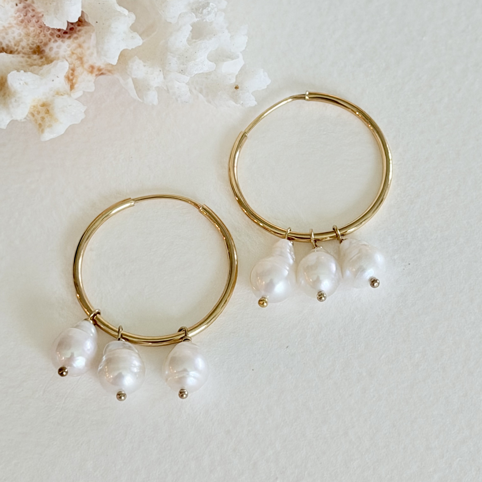 Gold hoop earrings with pearl drops on a light background