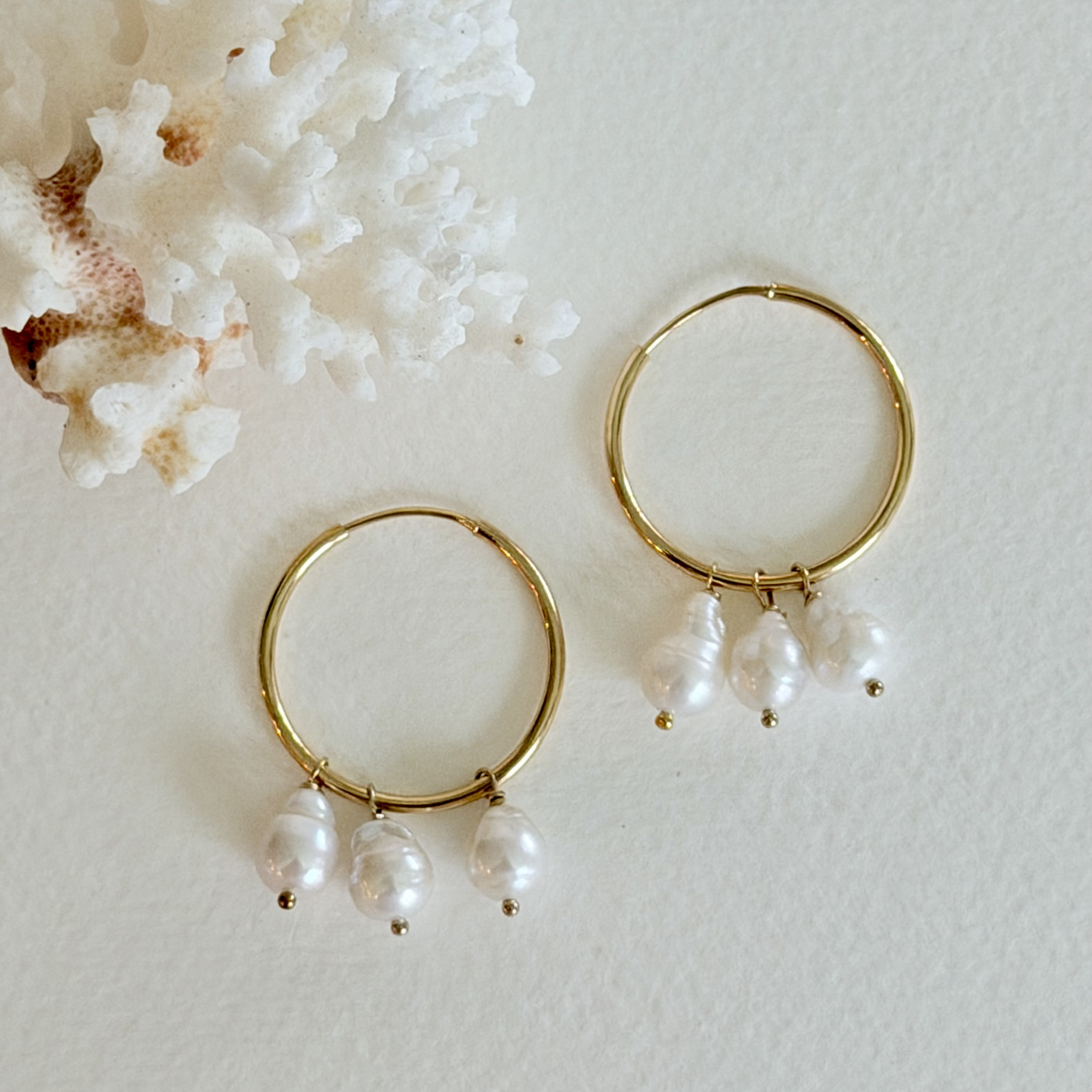 Gold hoop earrings with pearl drops on a textured white surface