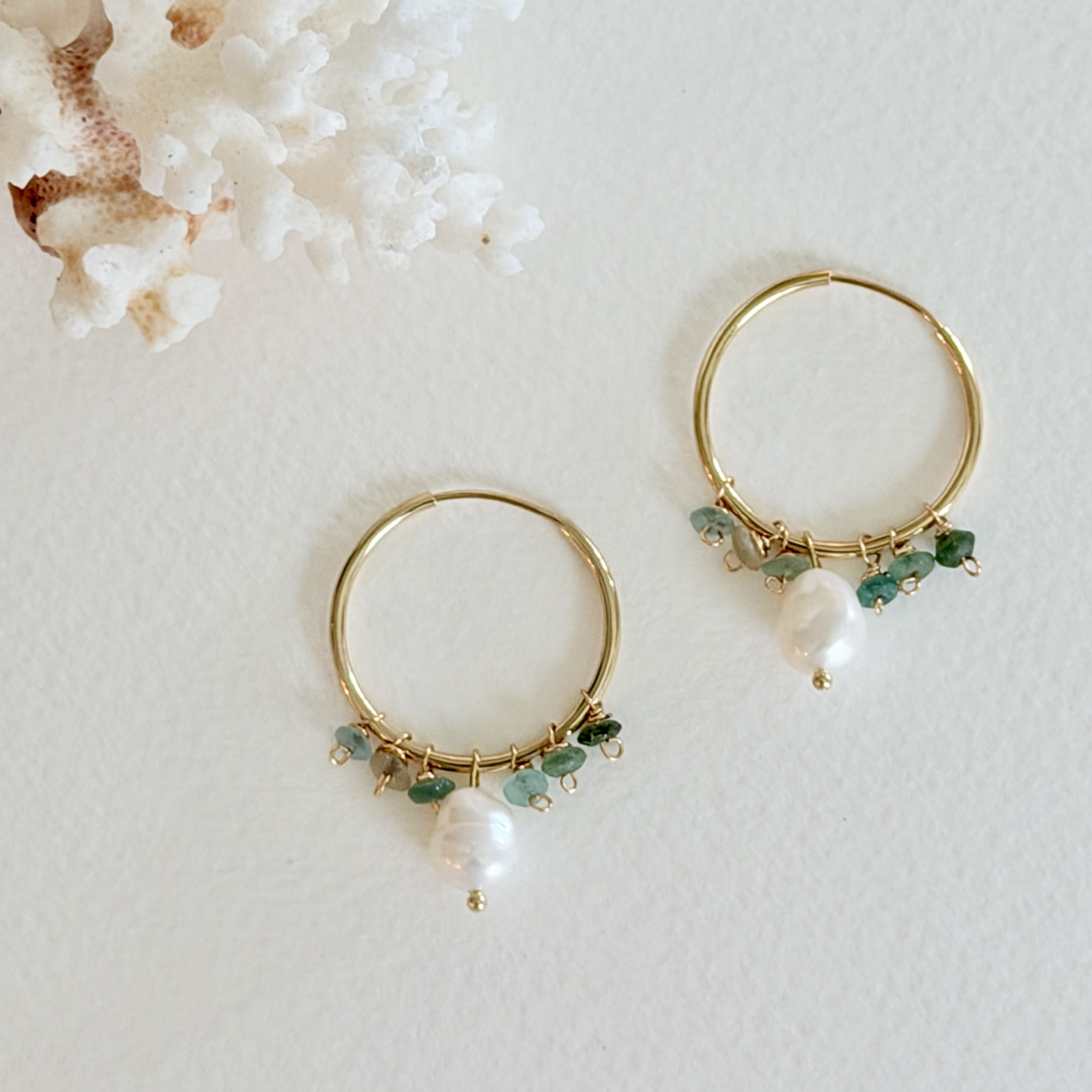 Gold hoop earrings with pearls and green beads on a light background