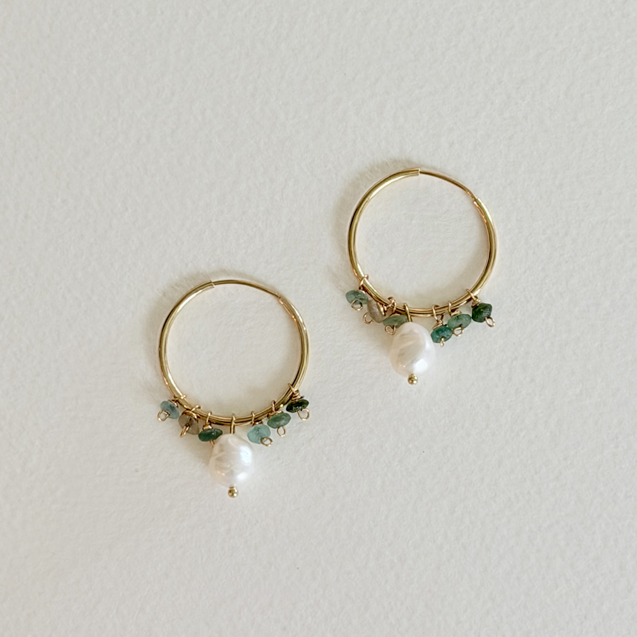 Gold hoop earrings with green beads and pearls on a light gray background