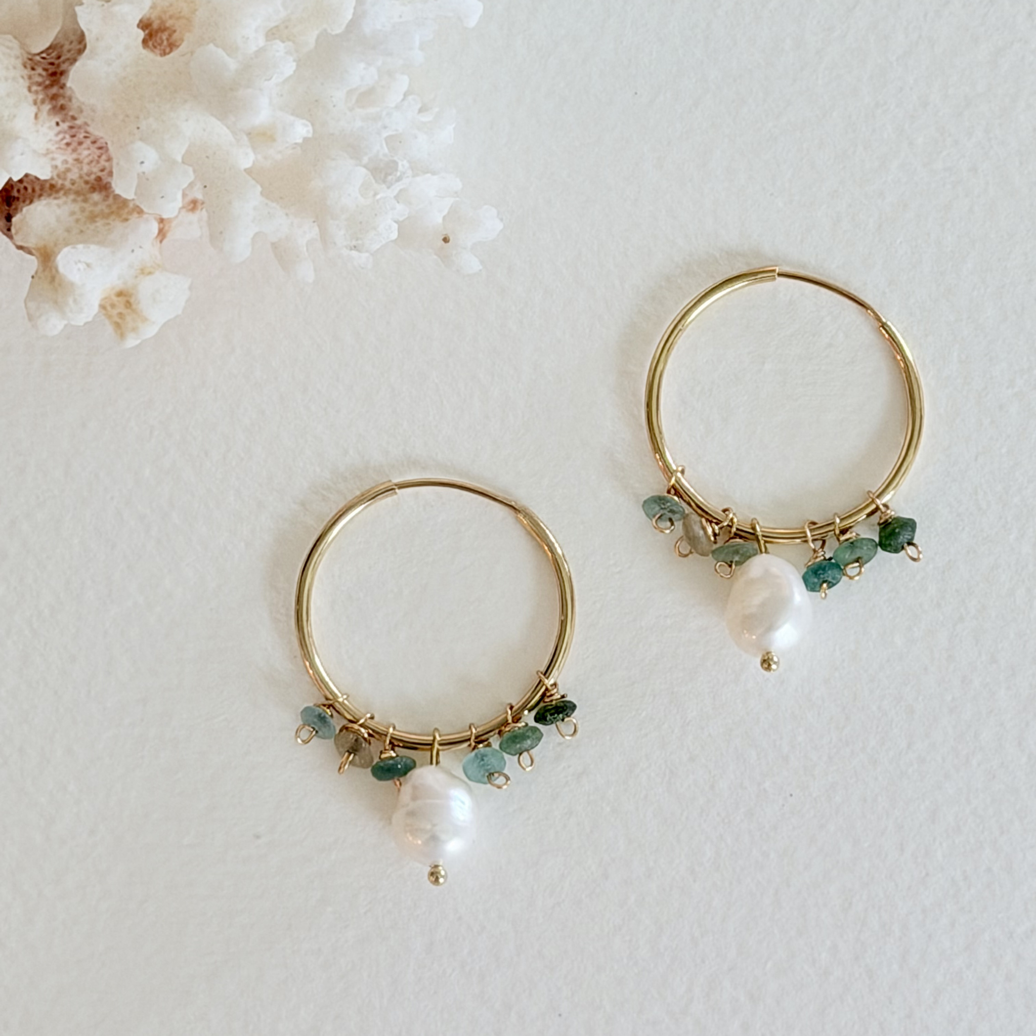 Gold hoop earrings with pearls and green beads on a light background