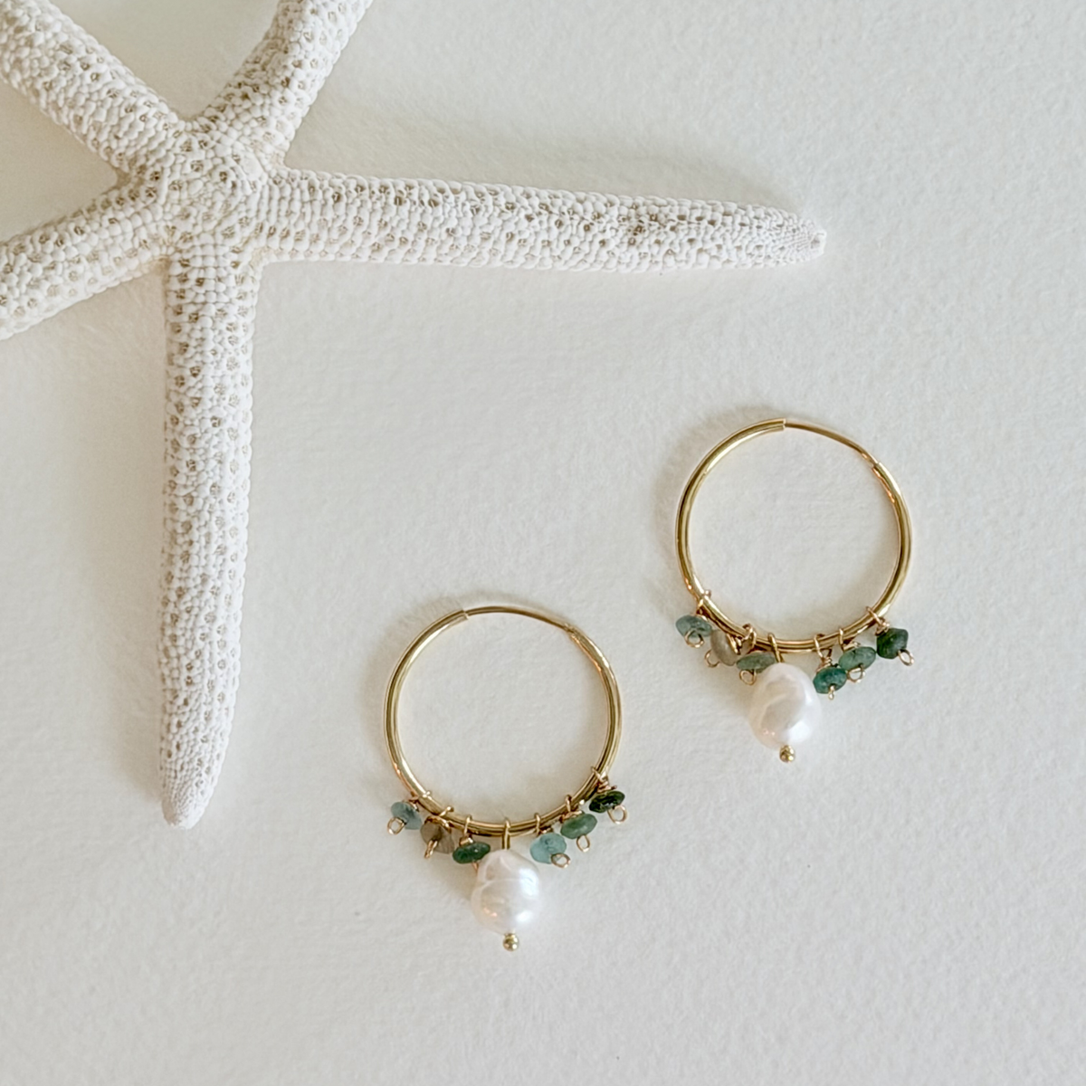 Gold hoop earrings with pearls and green beads on a light background with a starfish.