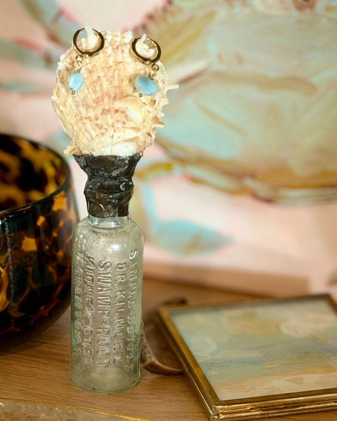 Larimar huggie earrings styled with seashell bottle and coastal painting