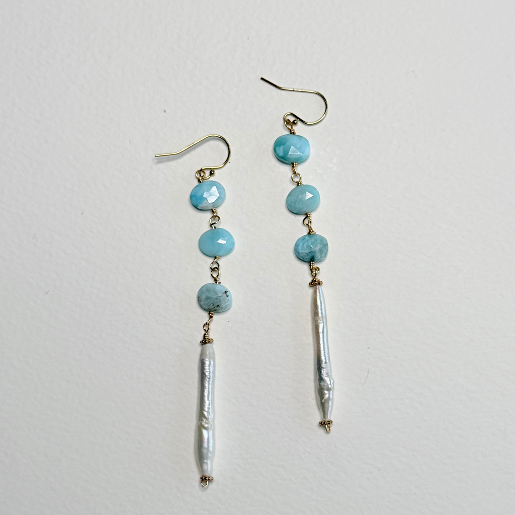 A pair of handmade dangle earrings featuring light blue larimar beads, gold-toned metal findings, and a dangling white pearl bead, displayed against a plain off-white background.
