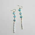 A pair of handmade dangle earrings featuring light blue larimar beads, gold-toned metal findings, and a dangling white pearl bead, displayed against a plain off-white background.