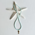 A beaded necklace with light aqua blue beads and a small gold mermaid tail charm, displayed on a white starfish prop against a white background.