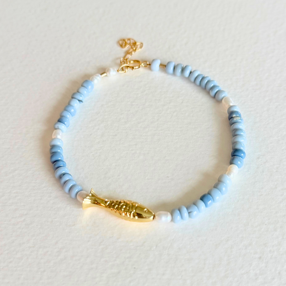 Bracelet with blue and white beads and gold accents on a light gray background
