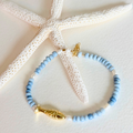Blue beaded bracelet with gold fish charm on a textured white surface