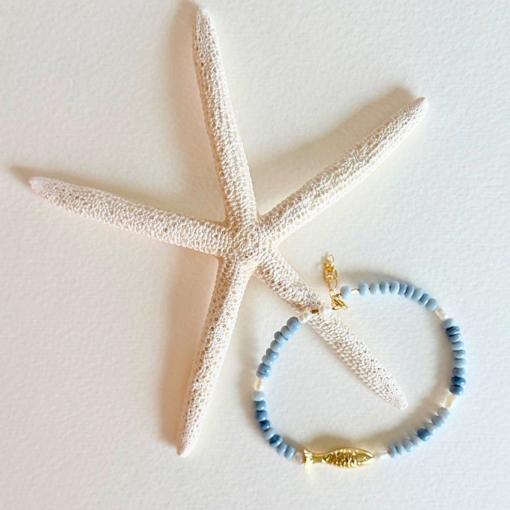 Blue beaded bracelet with a gold fish charm on a starfish