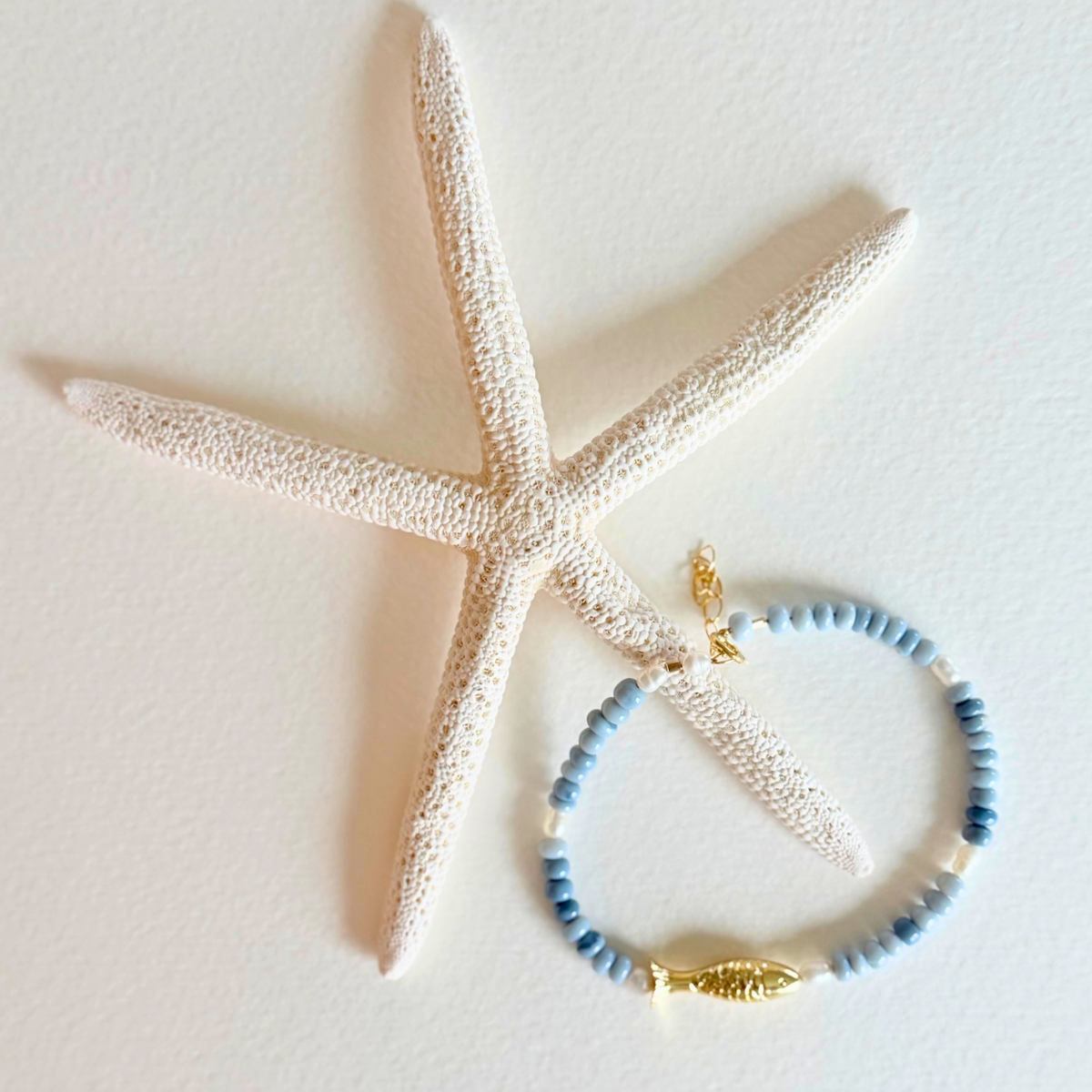 Blue beaded bracelet with a gold fish charm on a starfish
