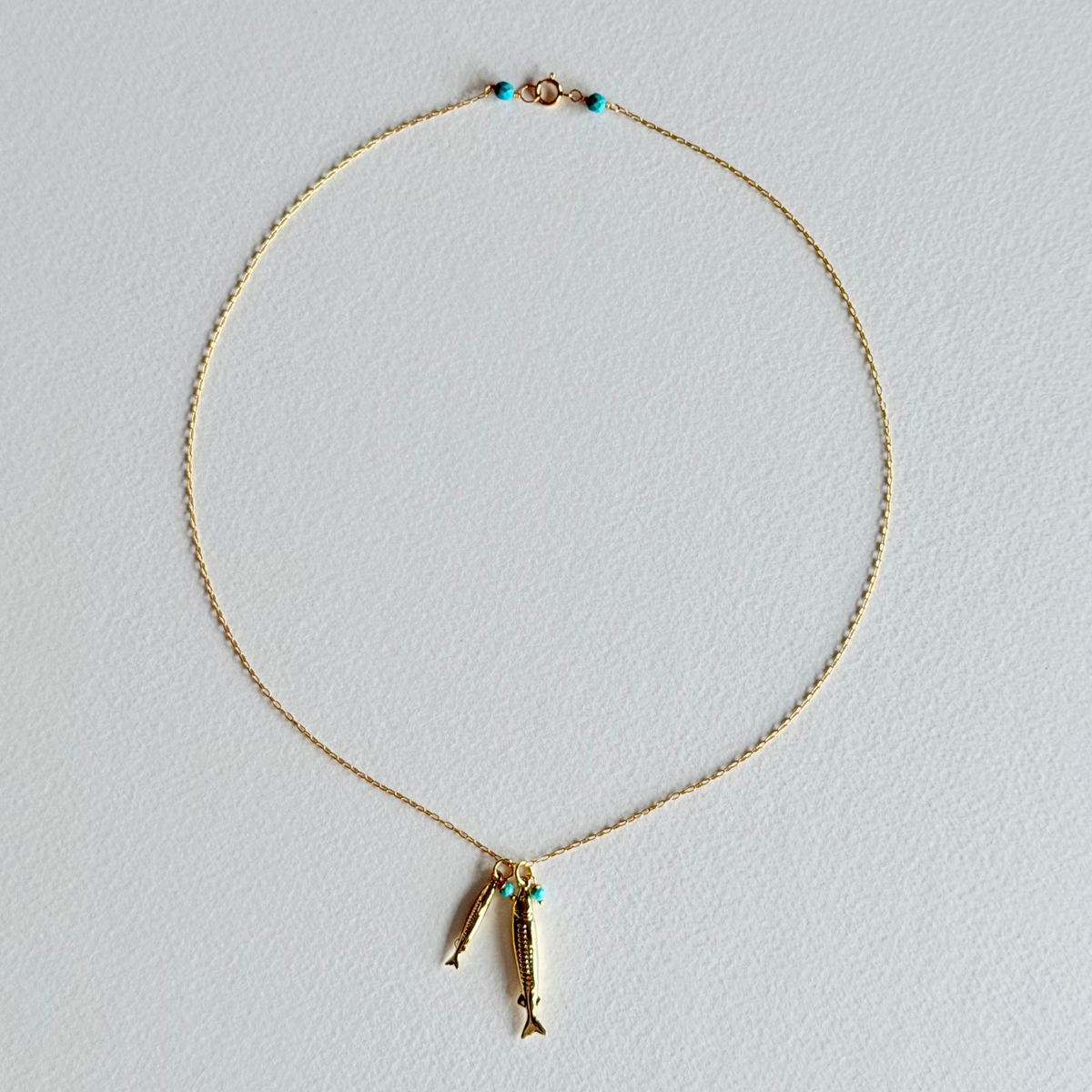 Gold necklace with fish-shaped pendants on a light gray background