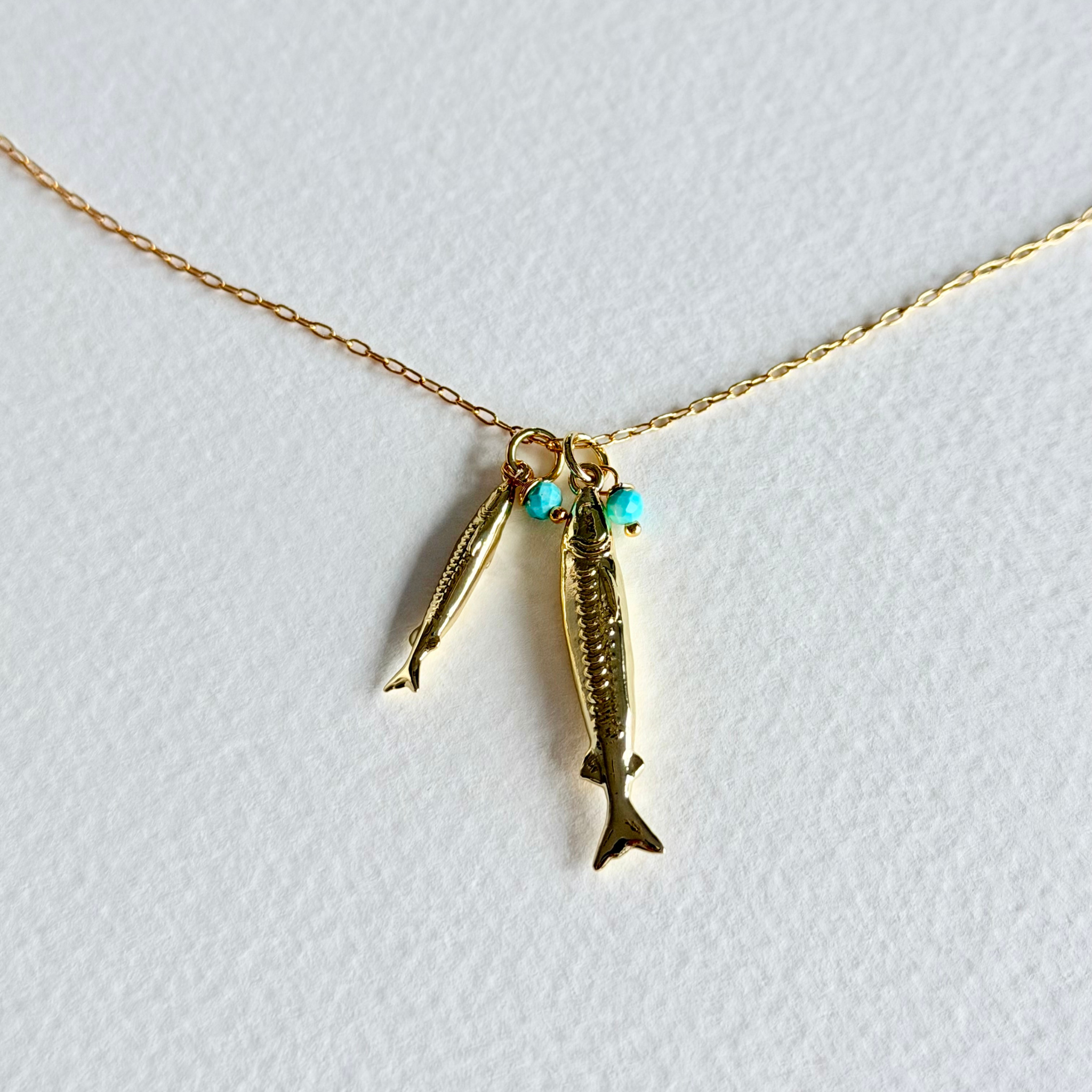 Gold fish-shaped pendant on a chain with turquoise beads against a light gray background
