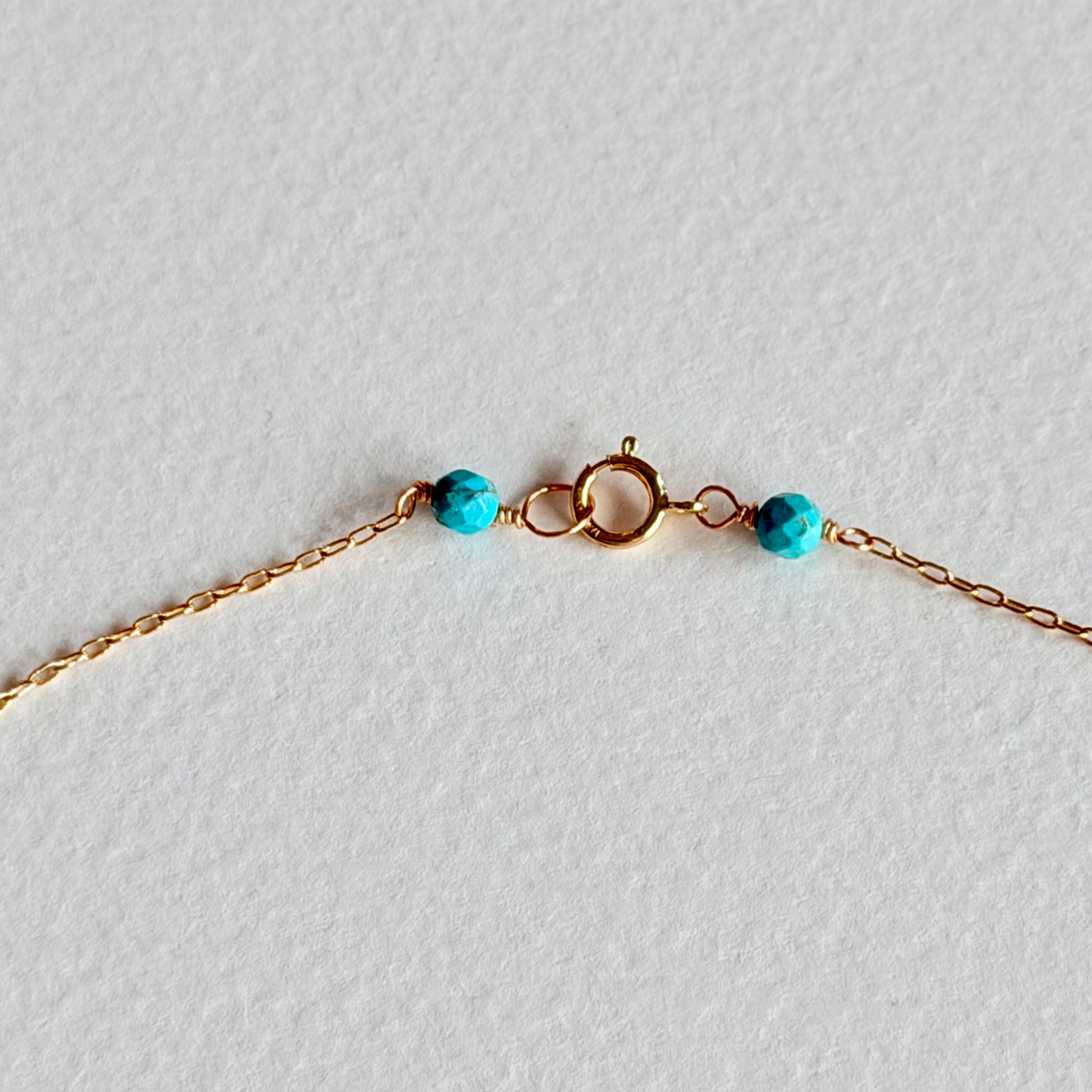 Gold bracelet with turquoise beads on a light gray background