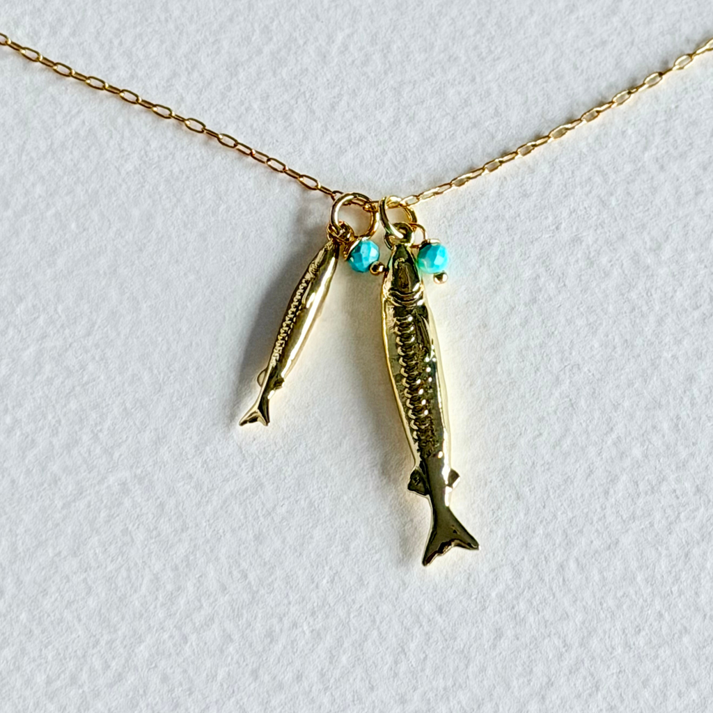 Gold fish-shaped pendant with turquoise beads on a gold chain against a white background
