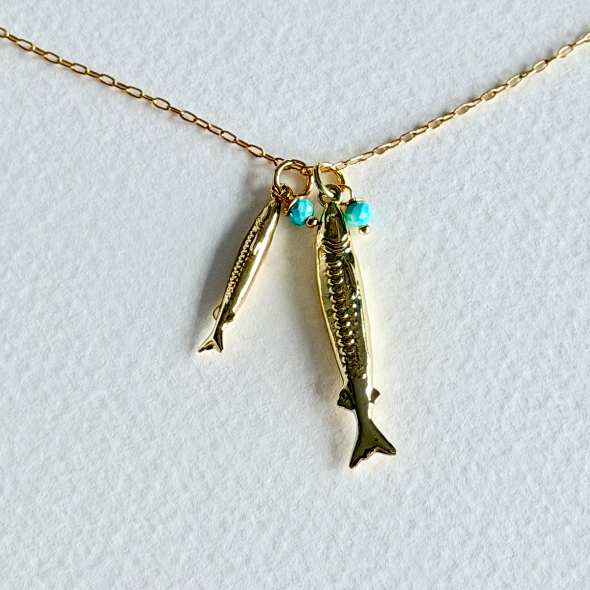 Gold fish-shaped pendant with turquoise beads on a gold chain against a white background