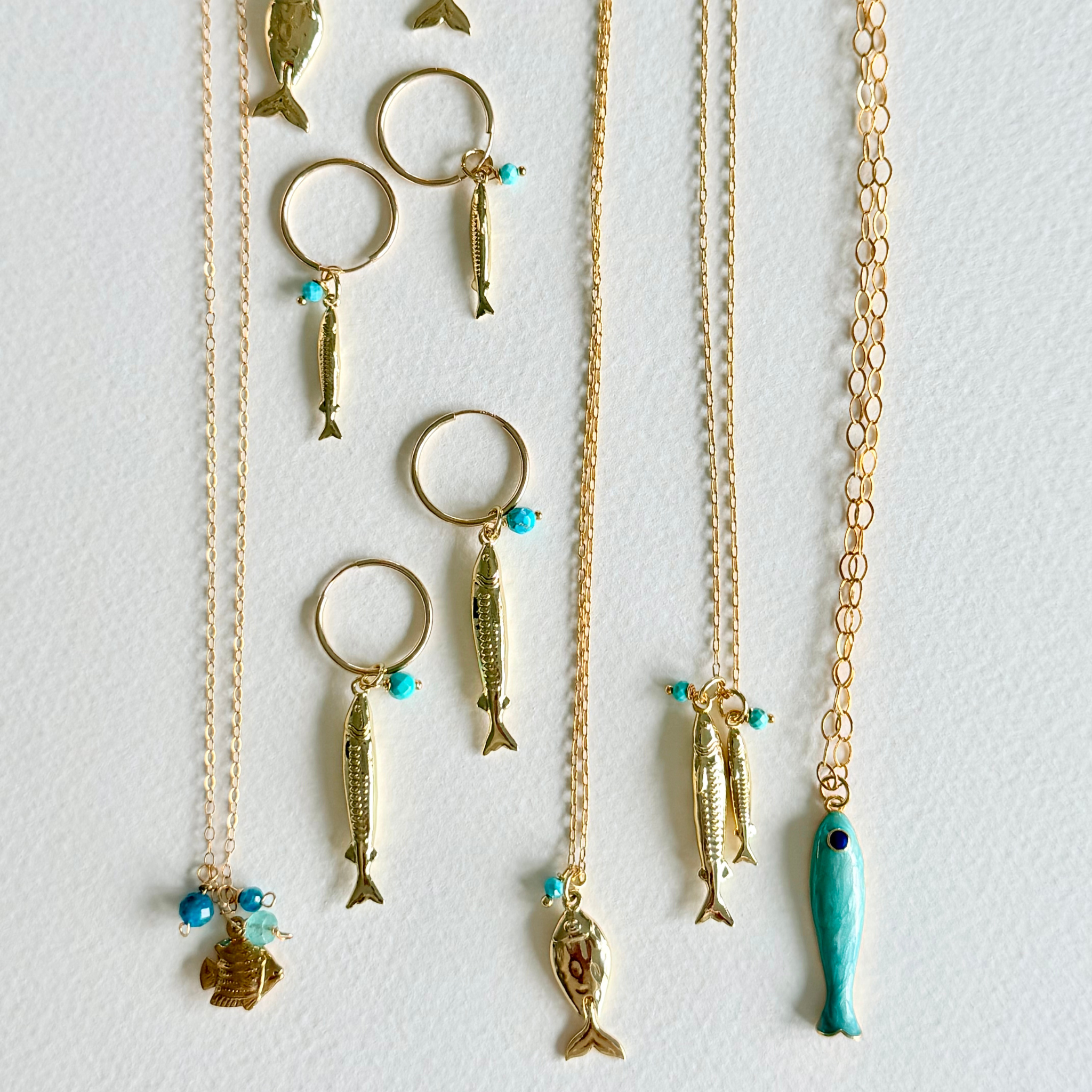 Gold necklaces with fish-shaped pendants on a light gray background